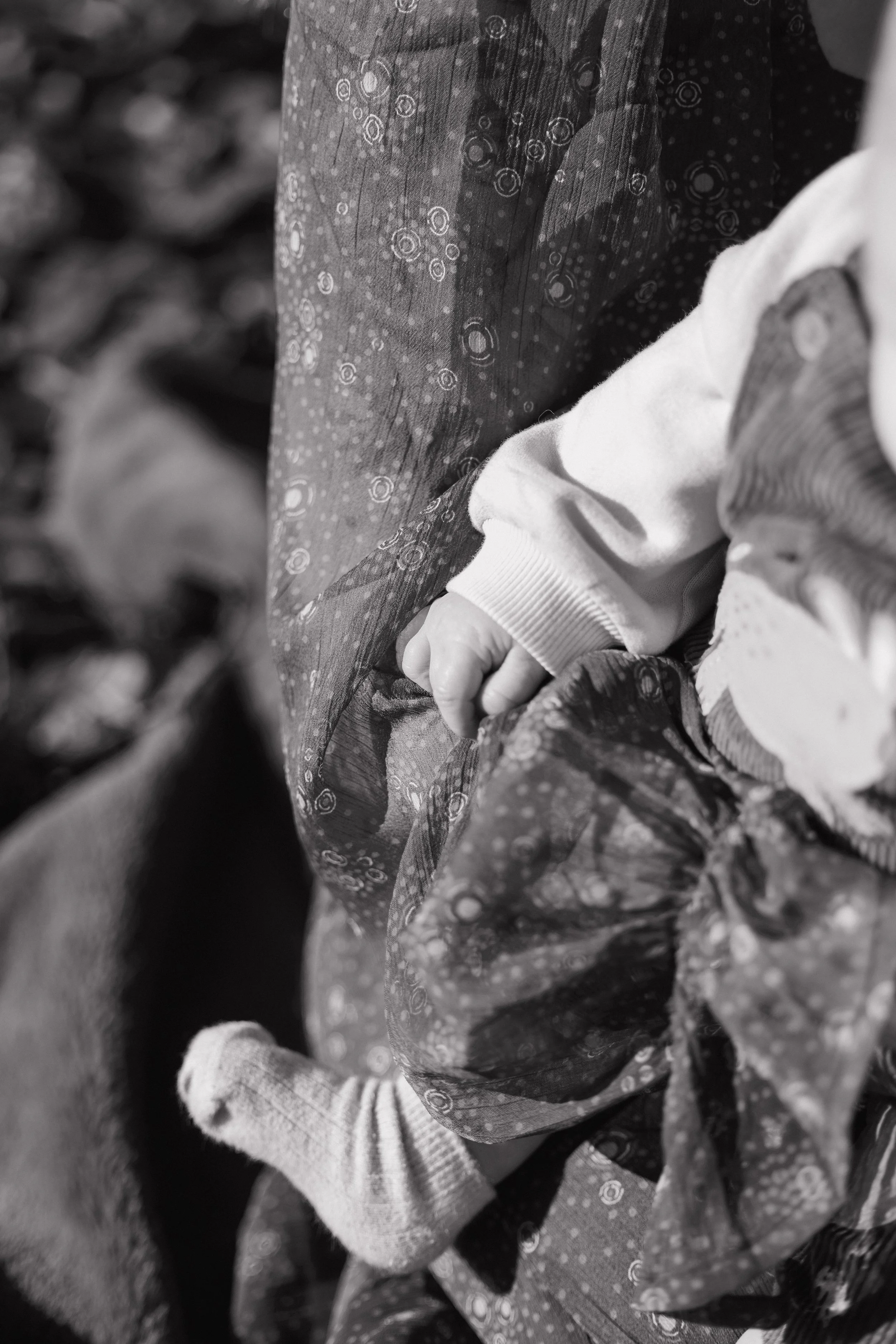 Close-up of a child's hand gripping an adult's clothing, both wearing patterned and plain clothing, in black and white.