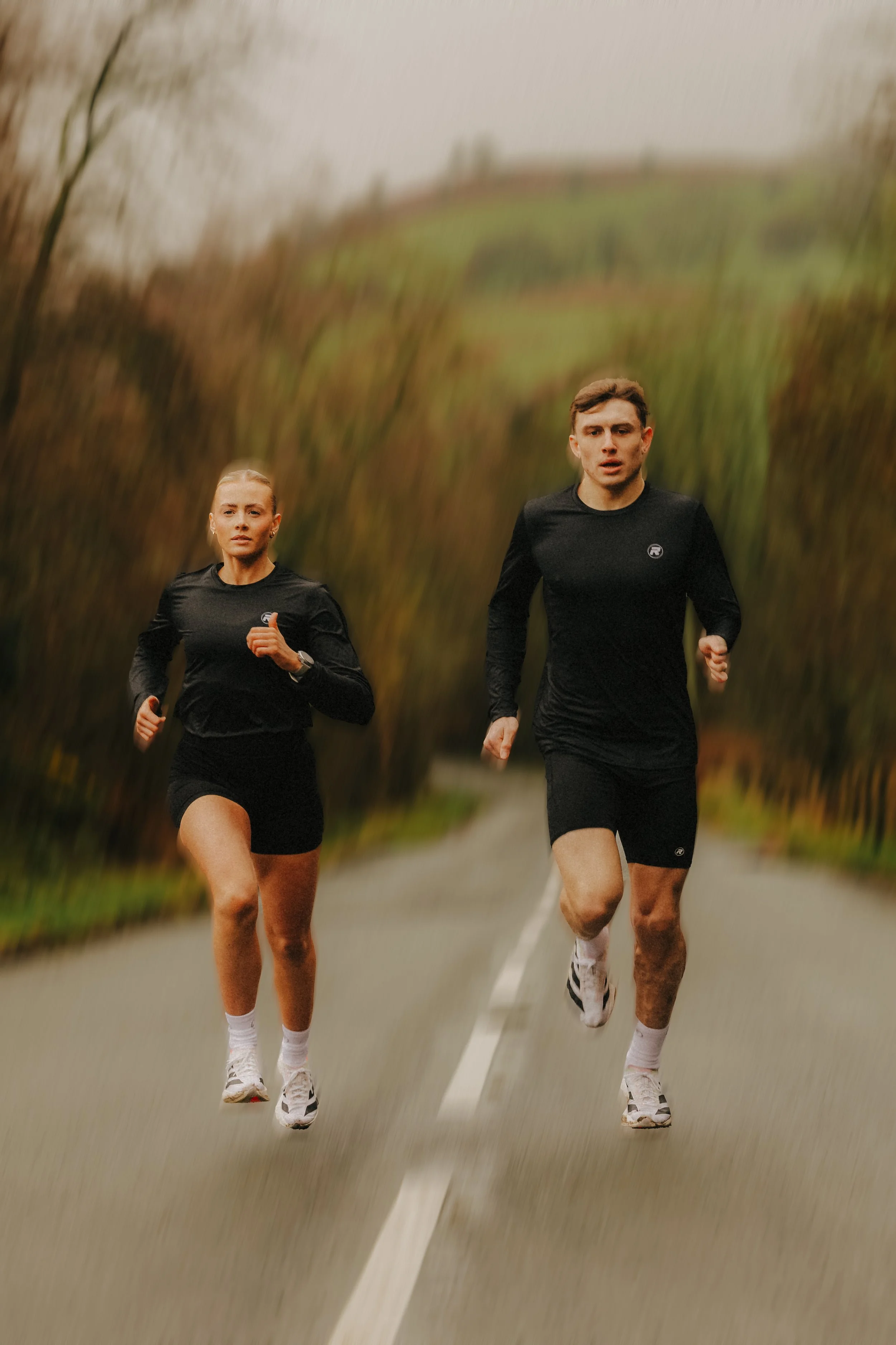 Two people running on a rural road surrounded by autumn trees.