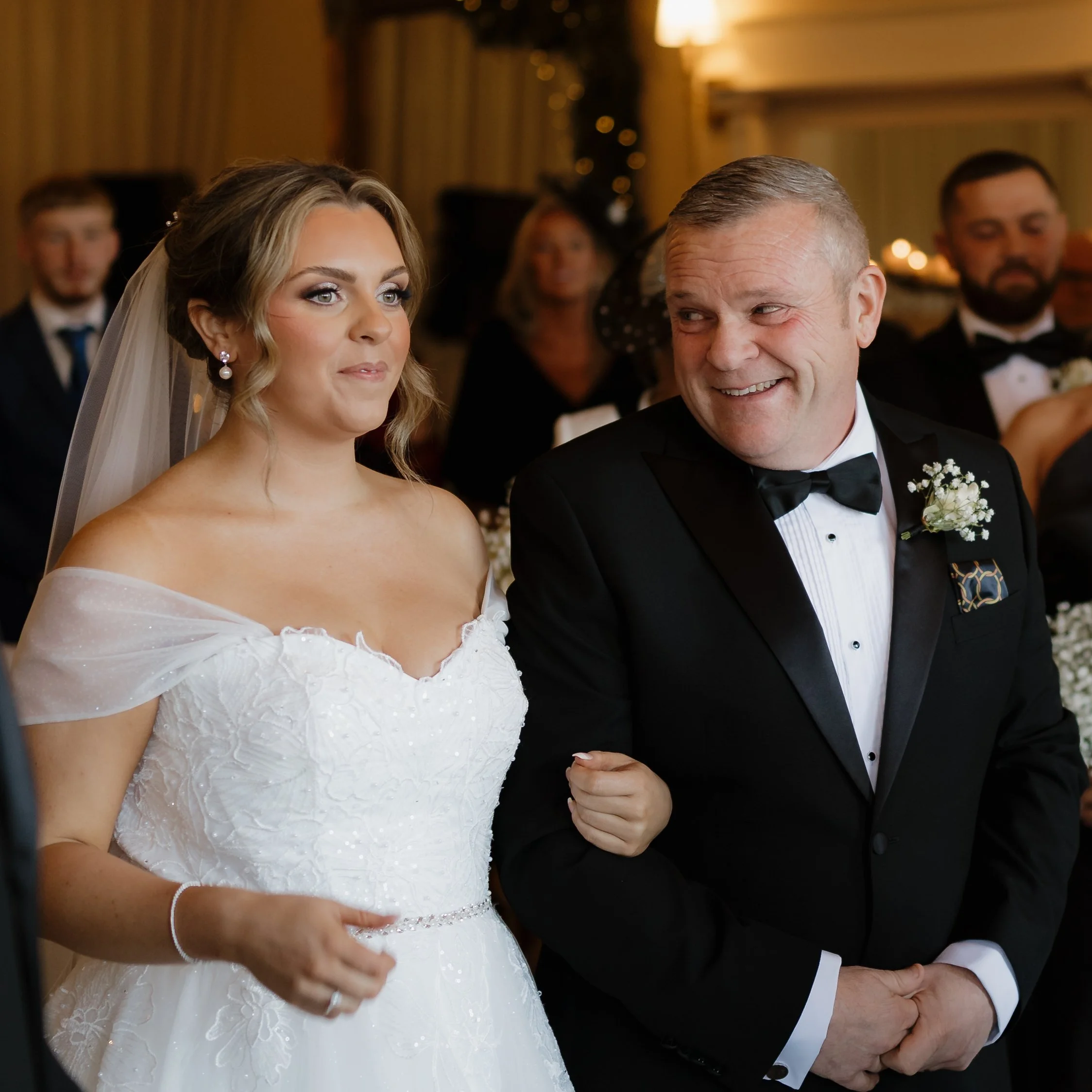 A bride in a white wedding dress holding onto an older man in a black tuxedo, during a wedding ceremony.