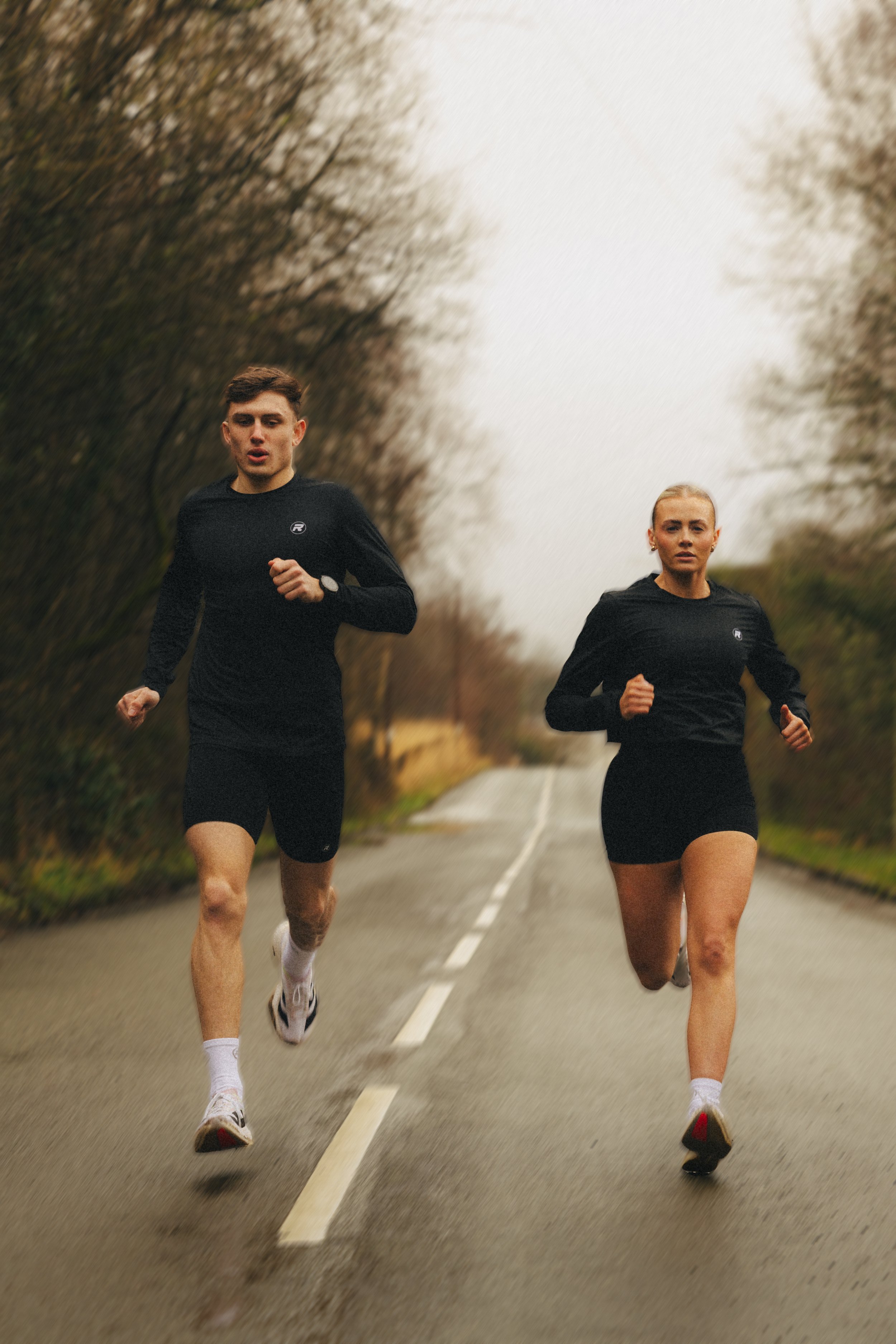 A man and woman running on a rural road with trees on both sides.