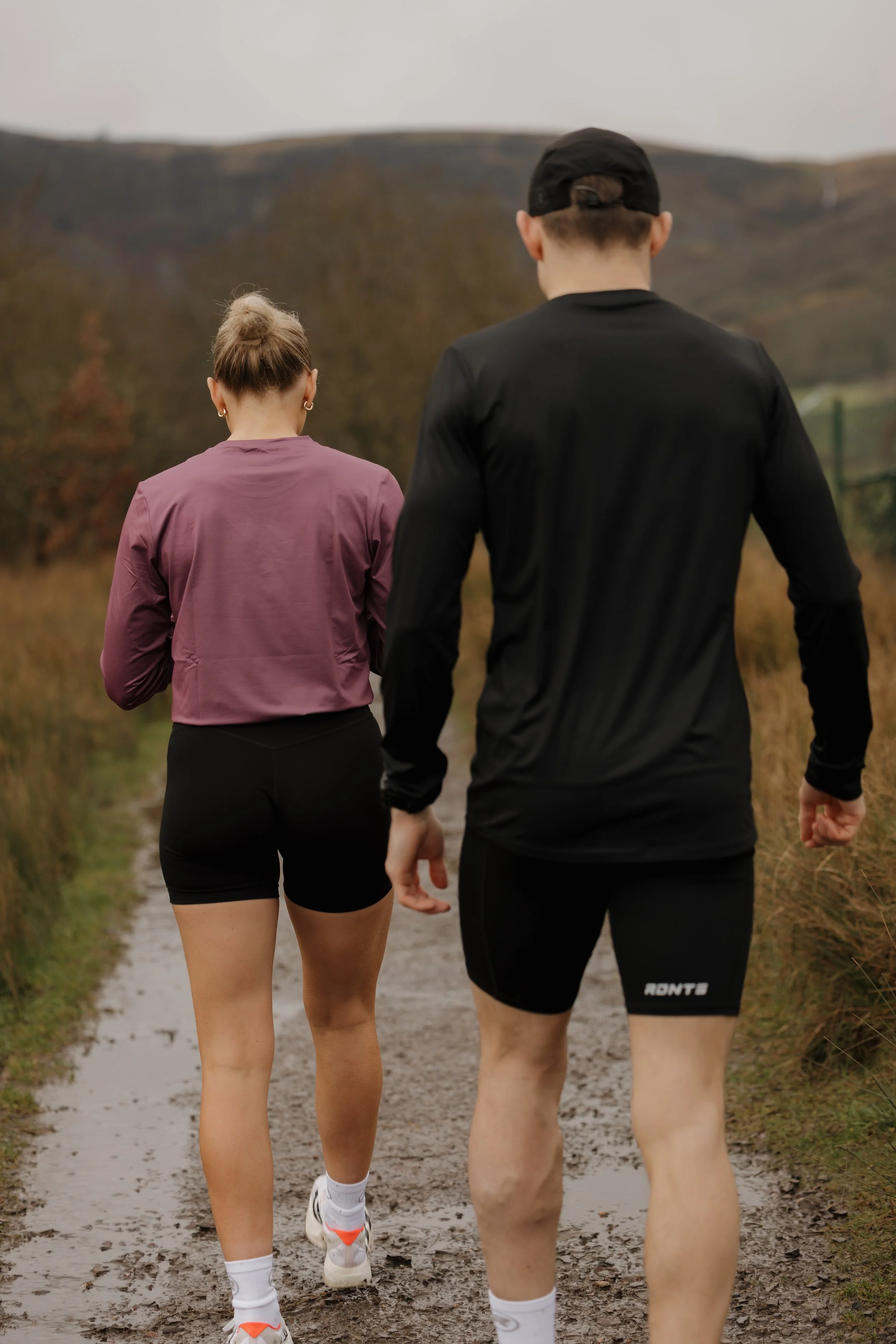 A woman and a man jogging together on a dirt trail in an outdoor rural setting during autumn.