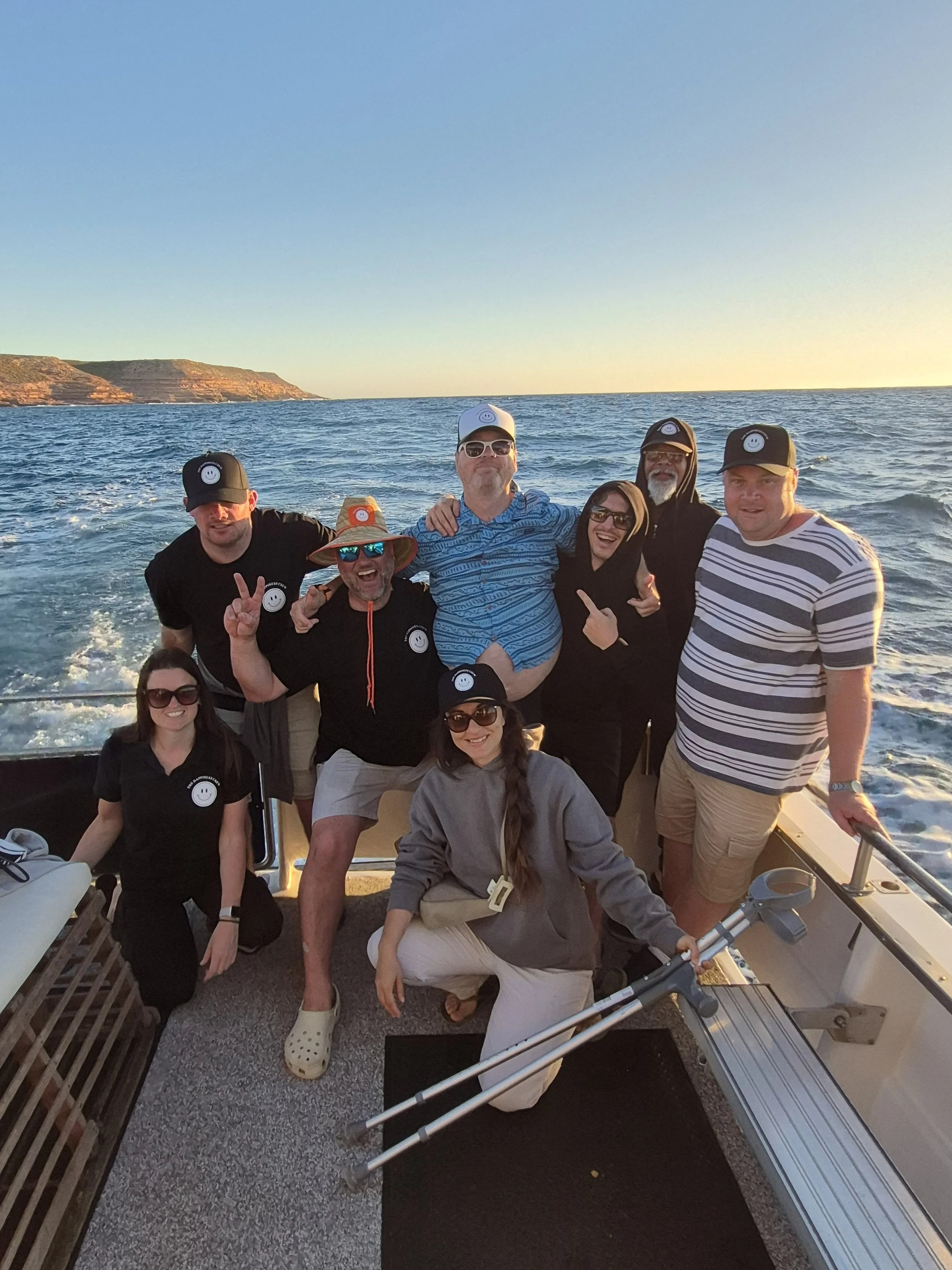 Group of people on a boat at sunset, smiling and posing for the photo.