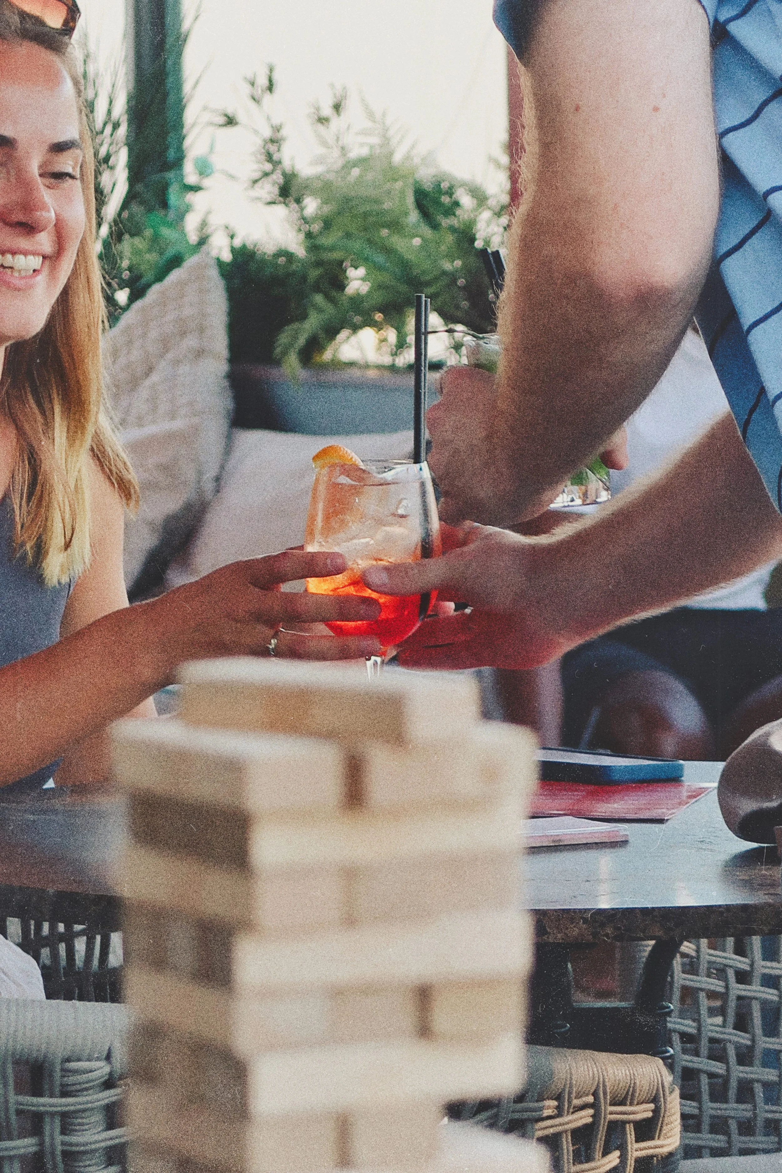 A woman smiling and holding a glass with an orange slice, with a man serving her a drink in a social setting.