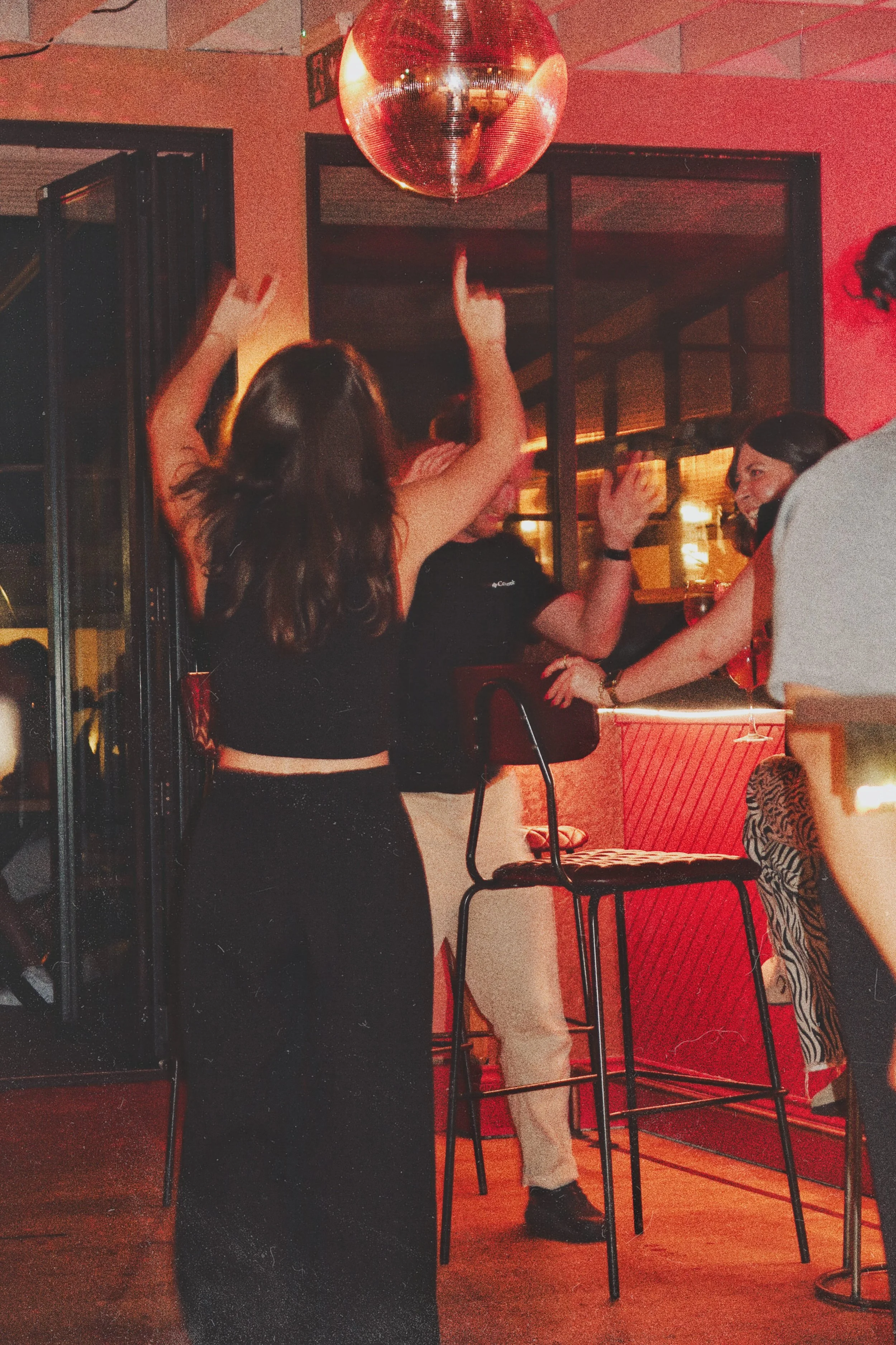 People dancing and socializing in a bar with a disco ball hanging from the ceiling, warm and lively atmosphere.