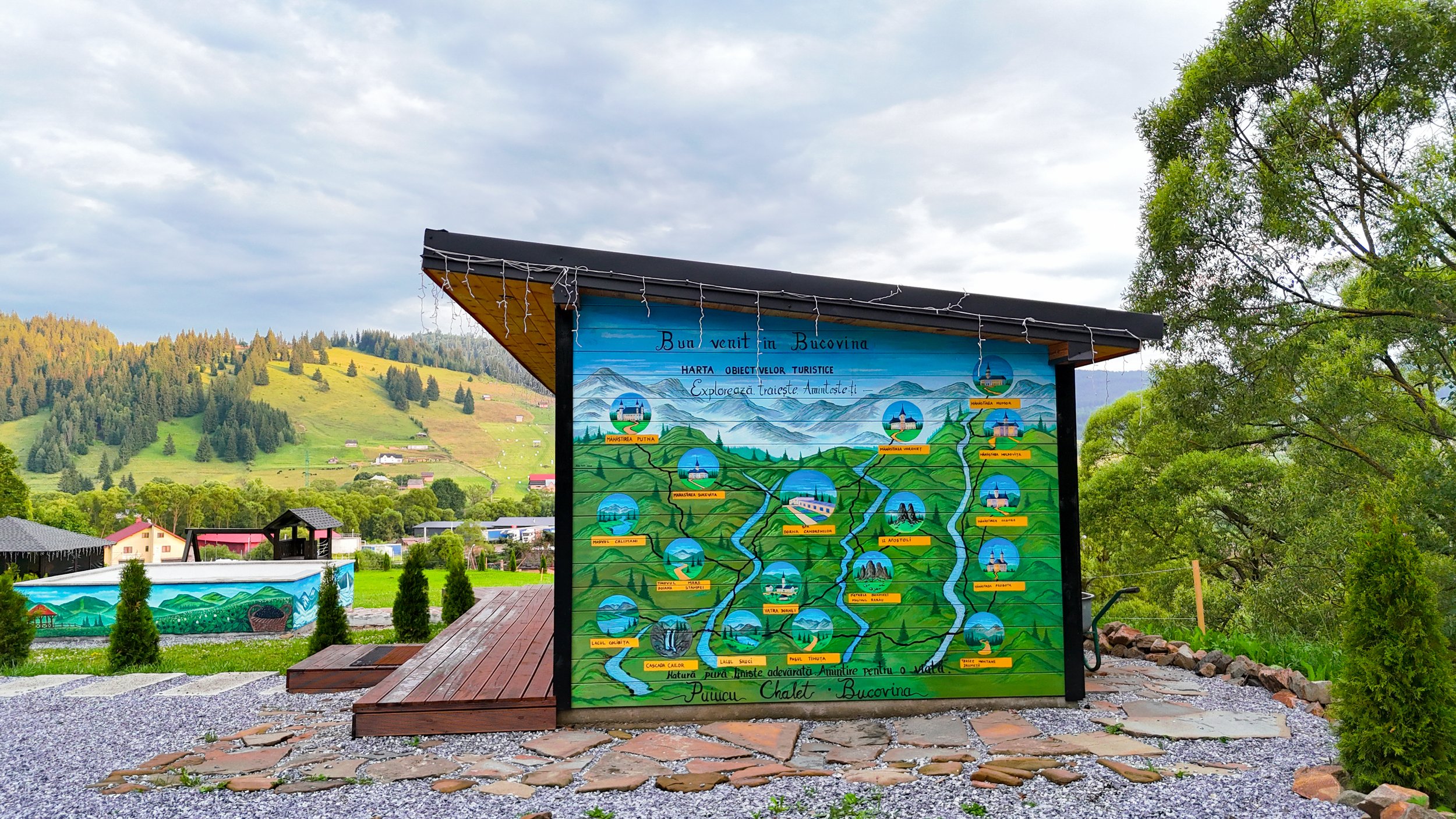 A colorful outdoor map display of Bucovina mountains and landmarks with hills, trees, and some houses in the background.
