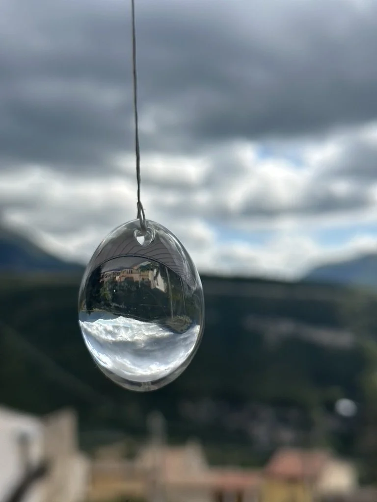Crystal yoni egg dangling with the reflection of clouds and ancient italian village inside.