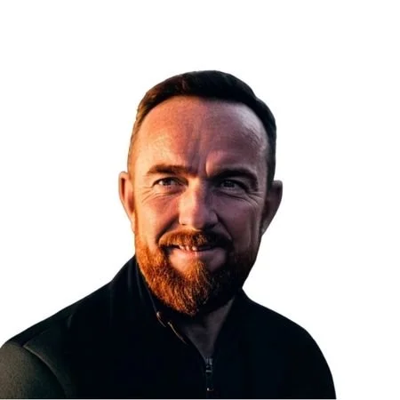 A man with short brown hair smiling, wearing a black zip up sweater..