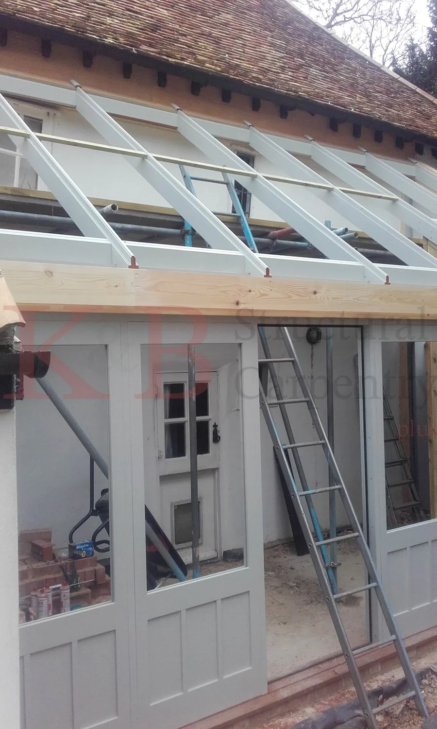 Under construction of a building extension with metal framing and wooden support beams, scaffolding, ladders, and construction tools.