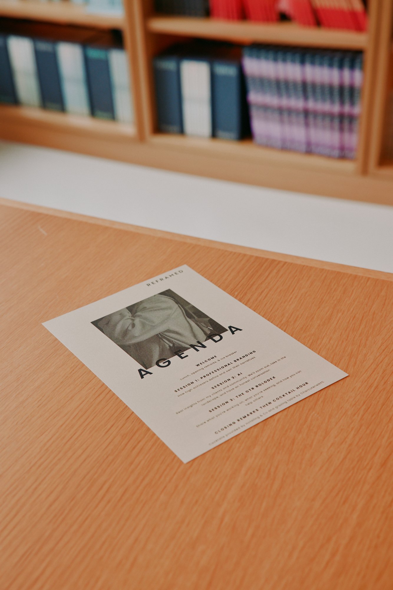 A flyer titled 'AGENDA' on a wooden table, with a bookshelf filled with books in the background.