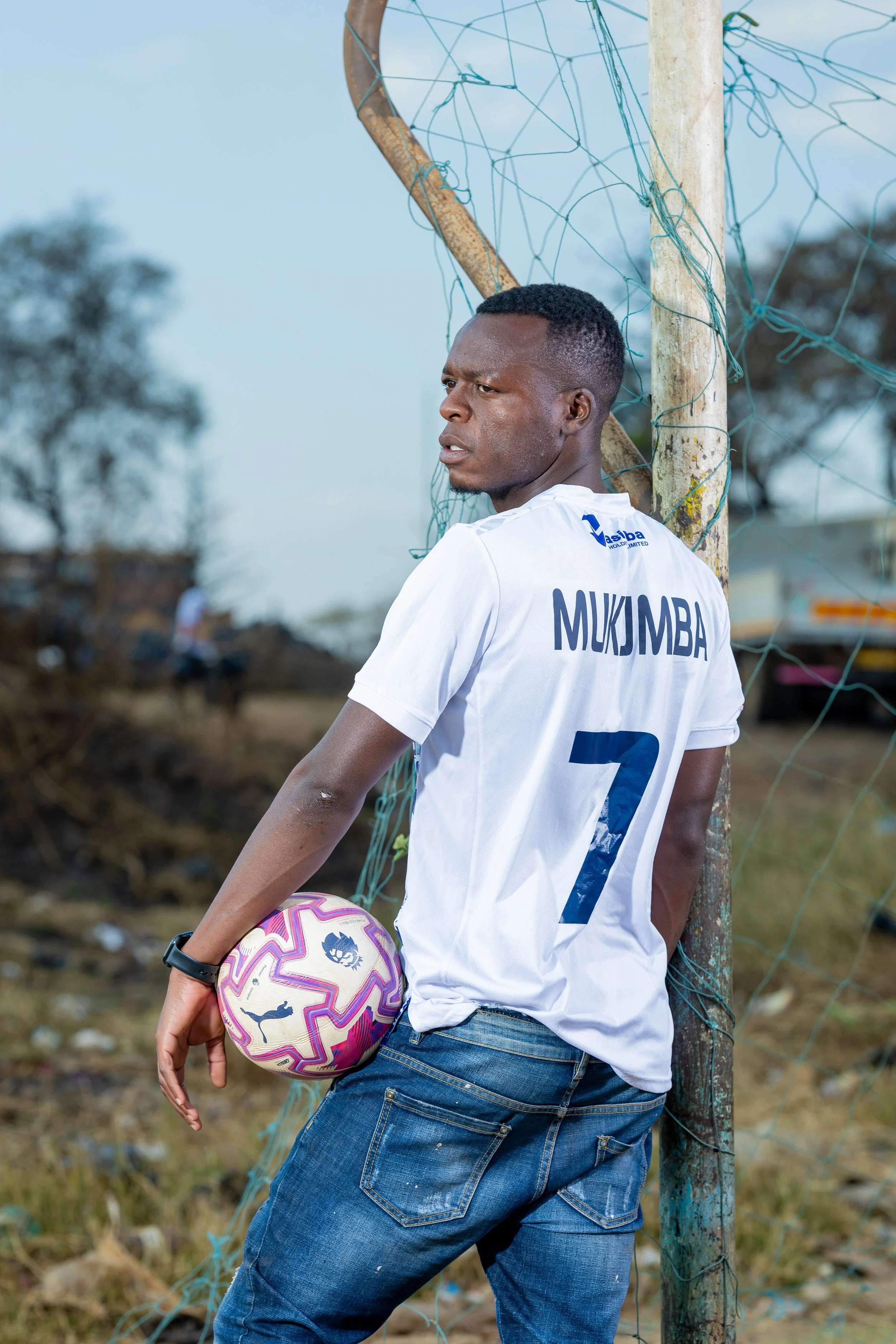 Marvellous Mukumba, wearing a shirt printed with his name and the number seven, leaning against a goalpost holding a football, photographed in Mbare, Harare