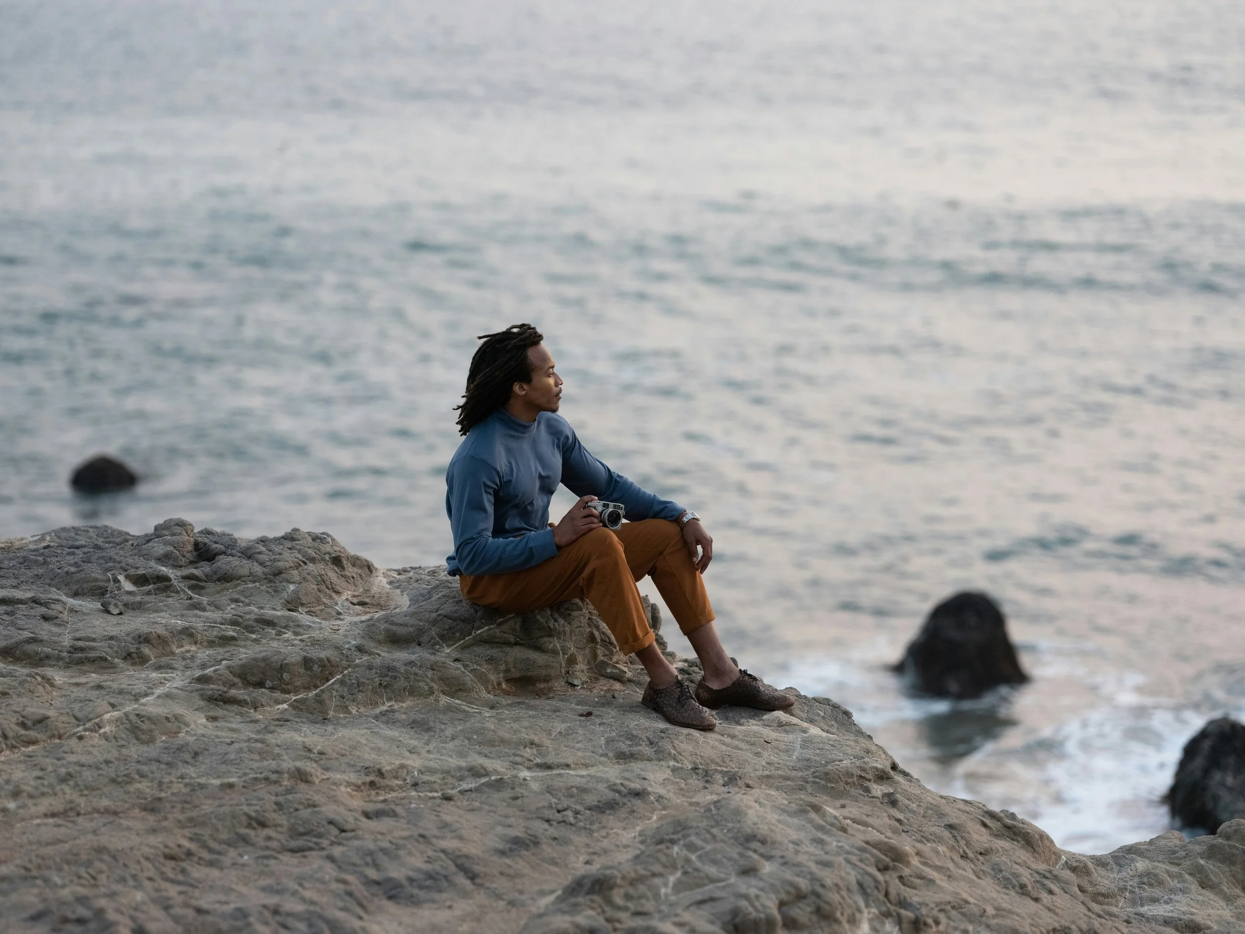 man sitting overlooking the ocean with a camera