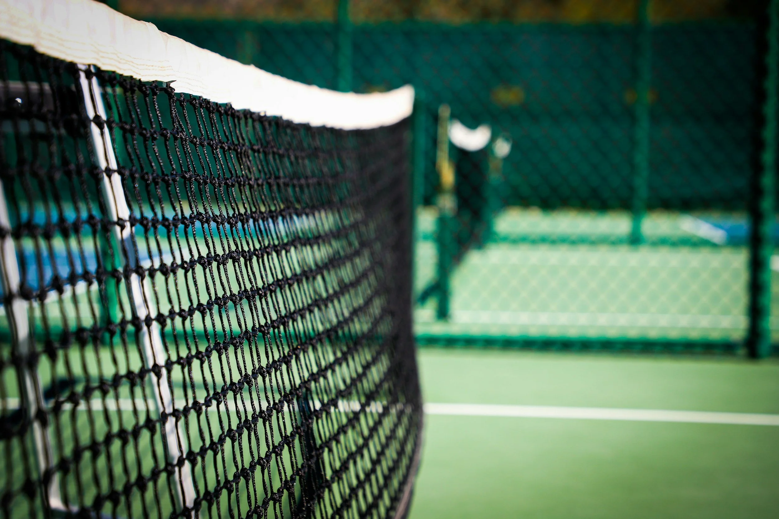 Close-up of a pickleball net on a green court with a blurred background of another court.