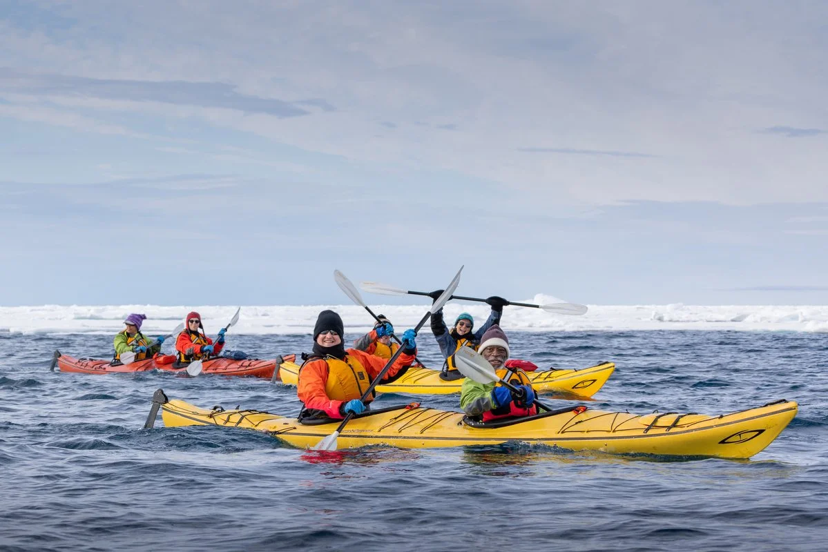 Travelers kayaking through Arctic water near the mountains of Svalbard on a polar expedition