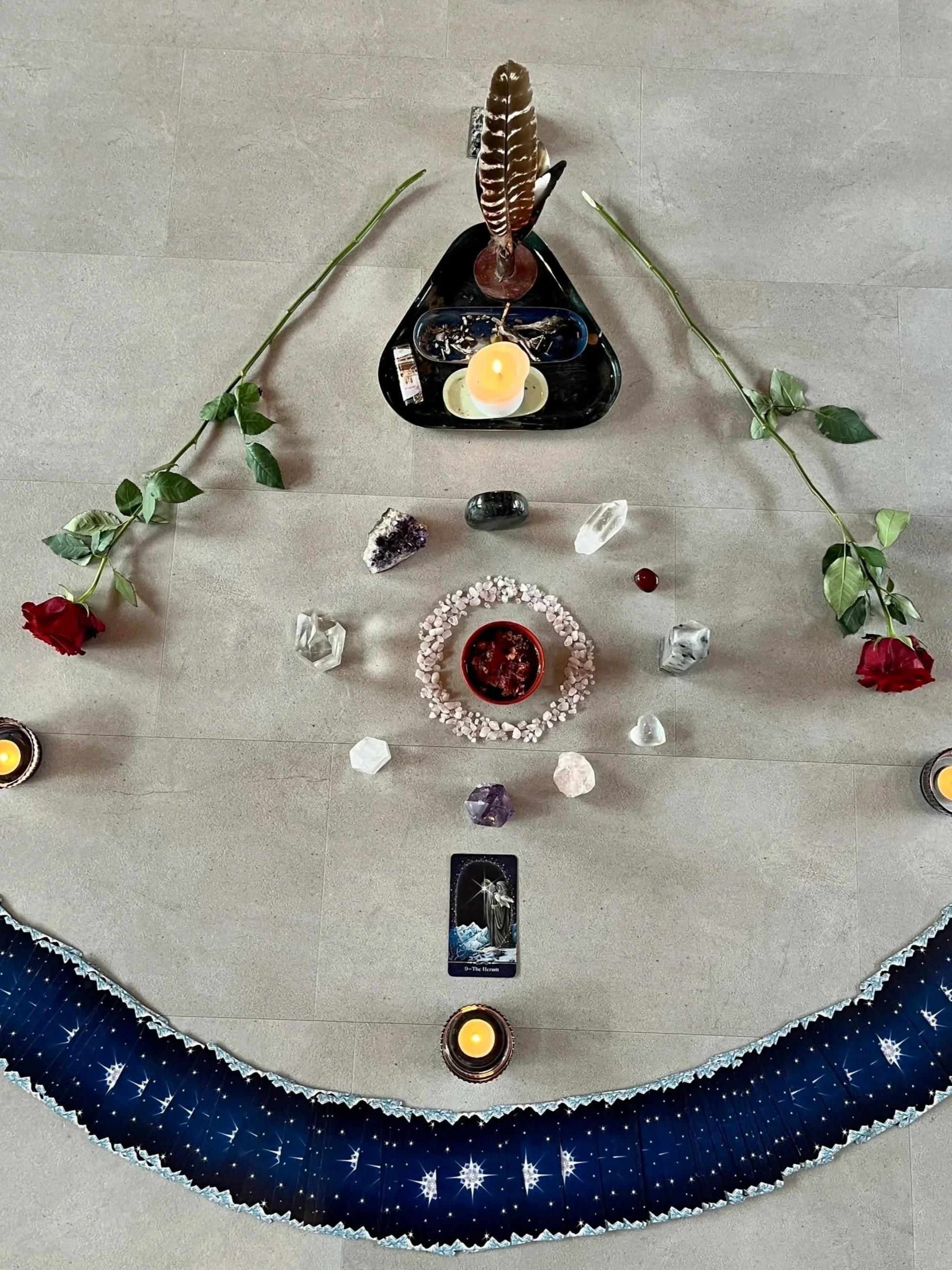 Ein spirituelles Mandala mit Kristallen, Kerzen, Blumen und Tarotkarte auf einem Boden. Das Mandala ist kreisförmig gestaltet mit verschiedenen Edelsteinen, Räucherstäbchen und Dekorationselementen.
