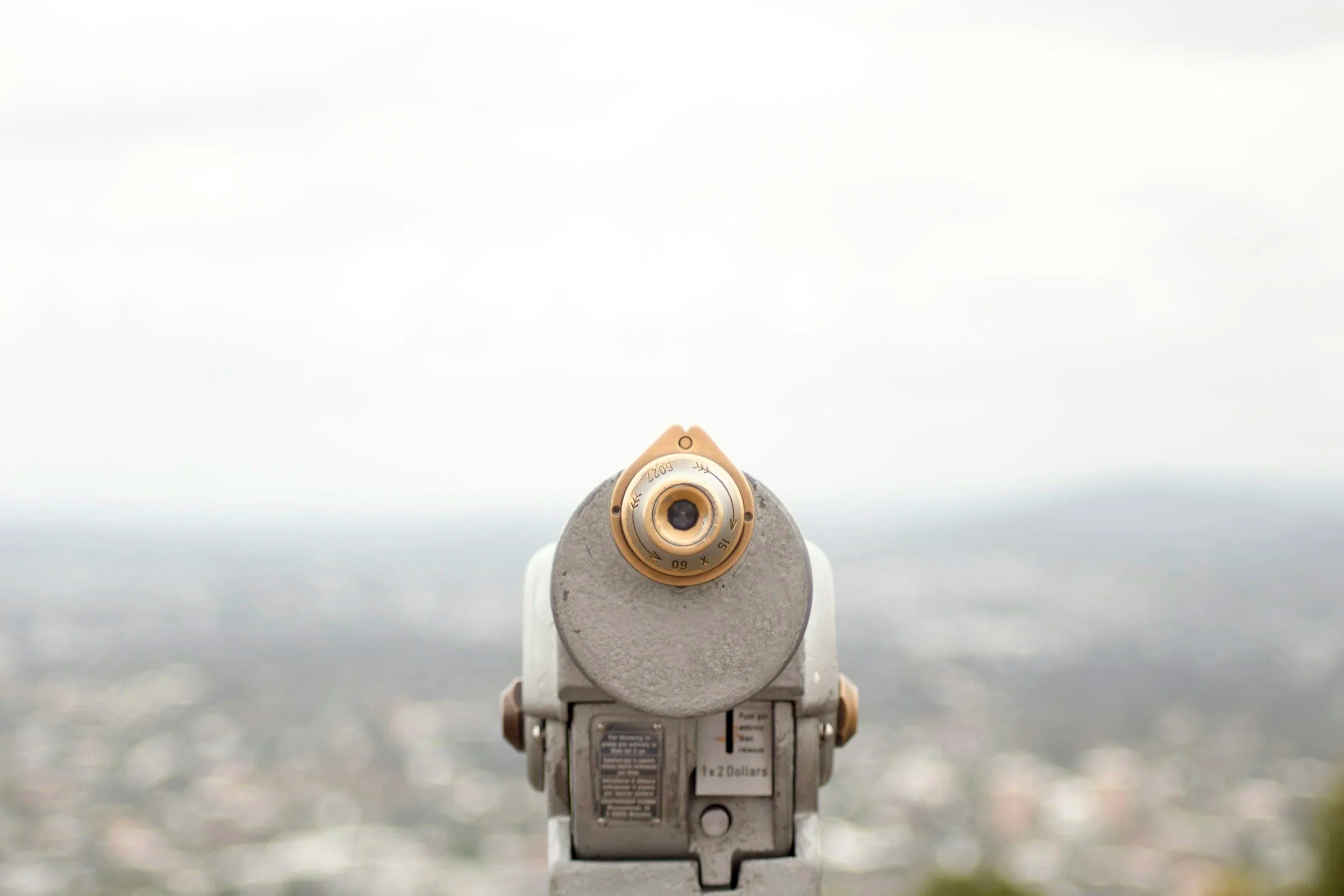 Looking through a coin-operated binocular viewer at a cityscape and cloudy sky.