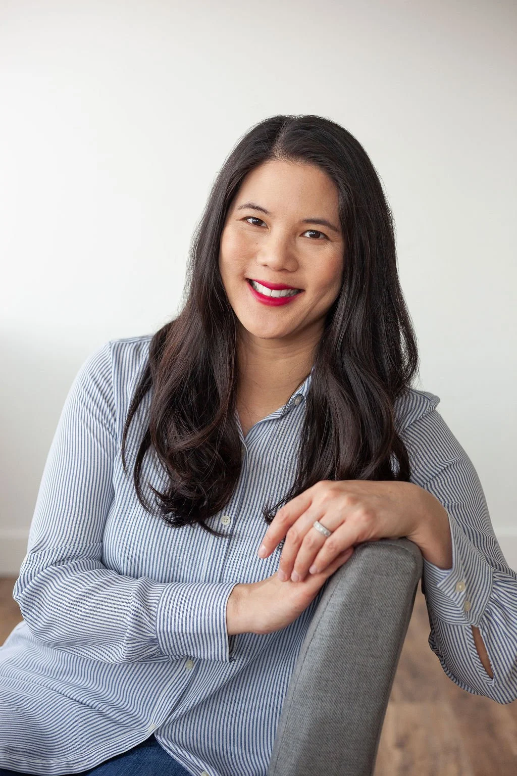 Asian female founder sitting in chair with blue and white stripped shirt