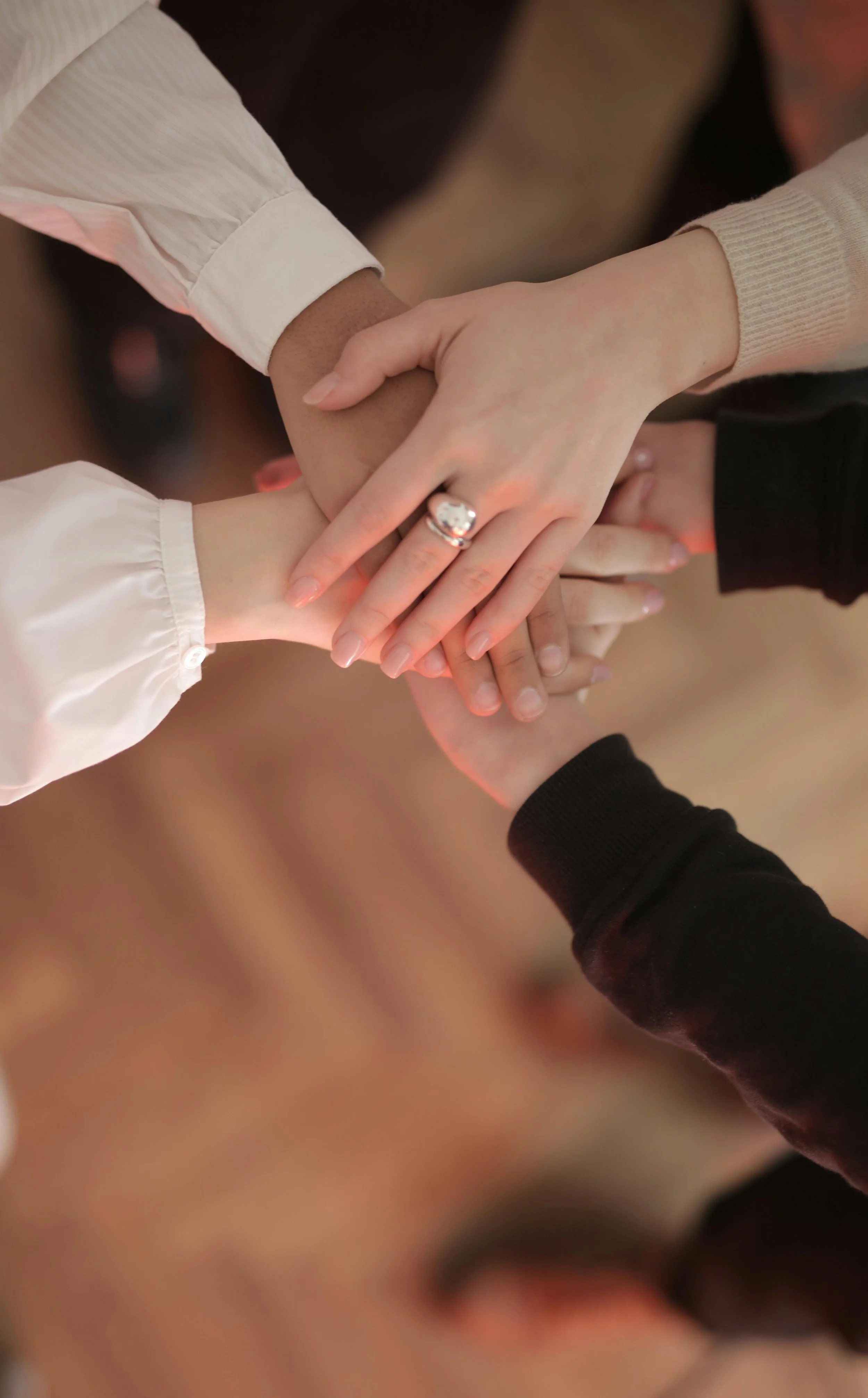 Multiple hands stacked together, symbolizing unity and teamwork, with one hand displaying an engagement ring.