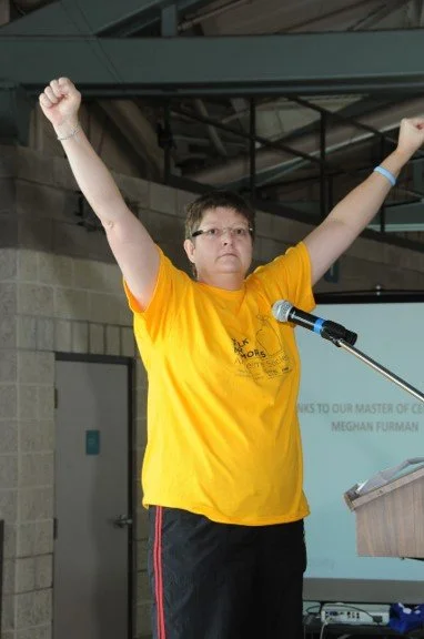 Person wearing a yellow T-shirt raising both arms during a presentation or event.