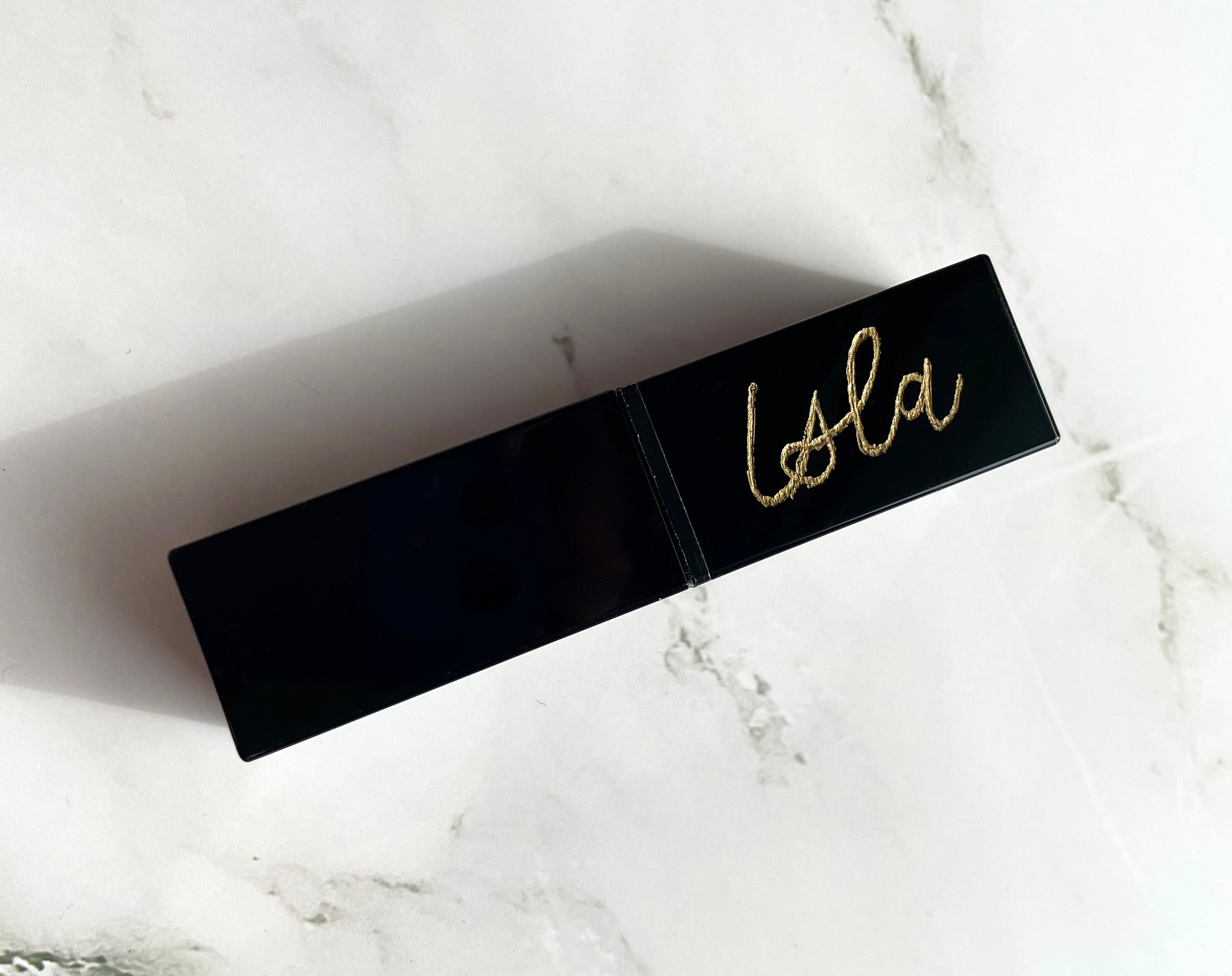 Black rectangular object with 'Isla' in gold script on a marble surface.