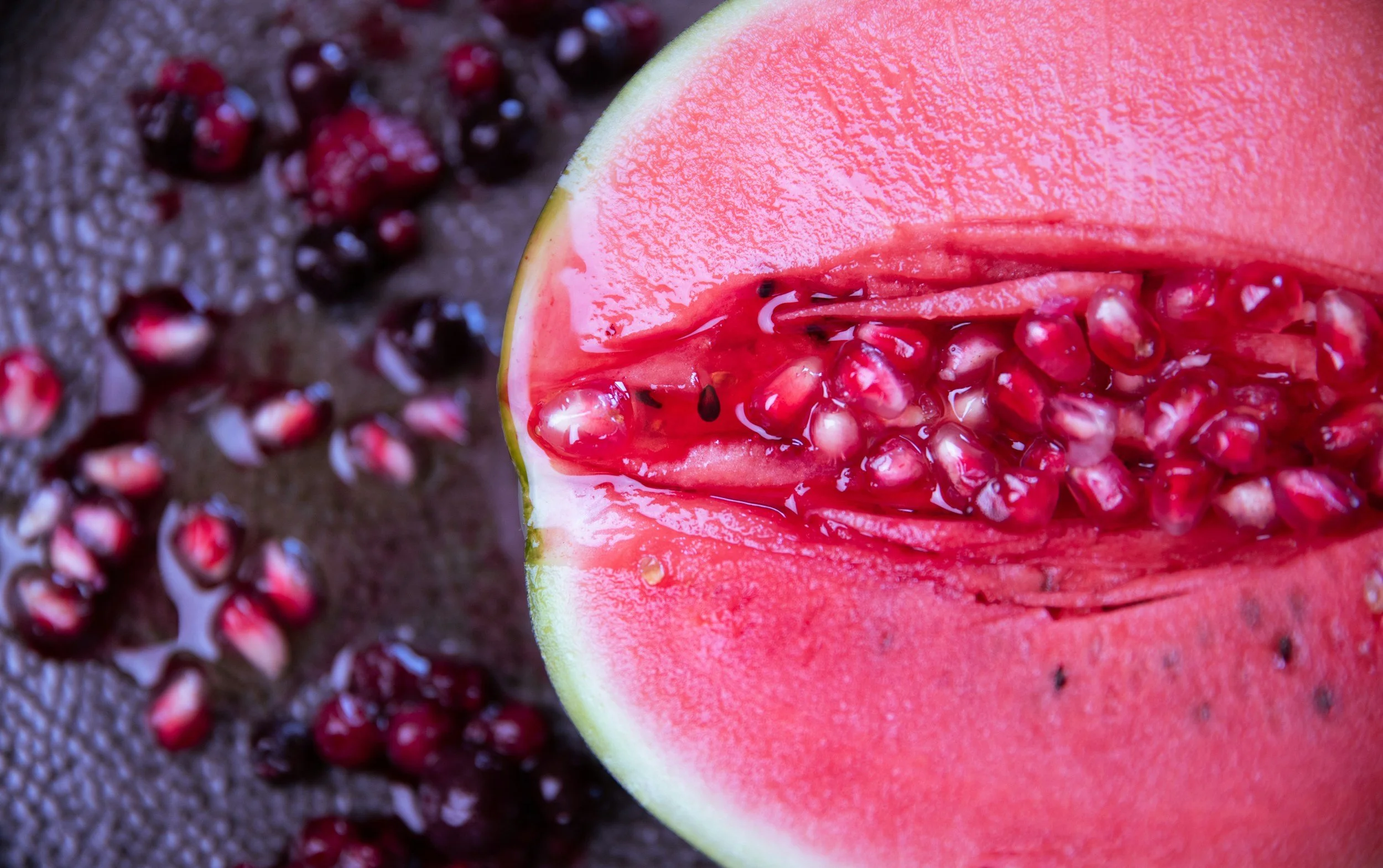 Close-up of a sliced watermelon with red seeds and vibrant pink flesh, on a textured surface, with loose seeds around it.