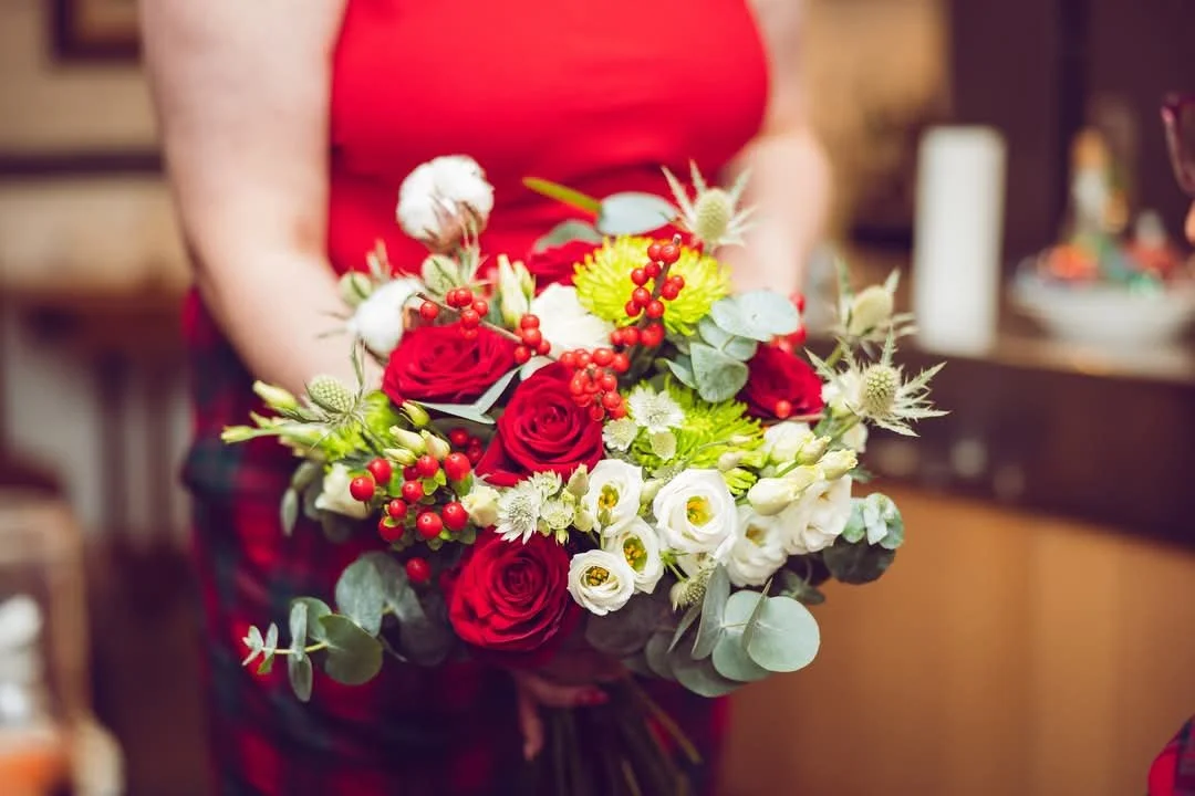 Person holding a bouquet of red and white flowers with green foliage in an indoor setting.