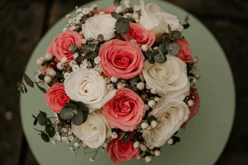 A bouquet of pink and white roses with greenery and small white berries on a light green circular surface.