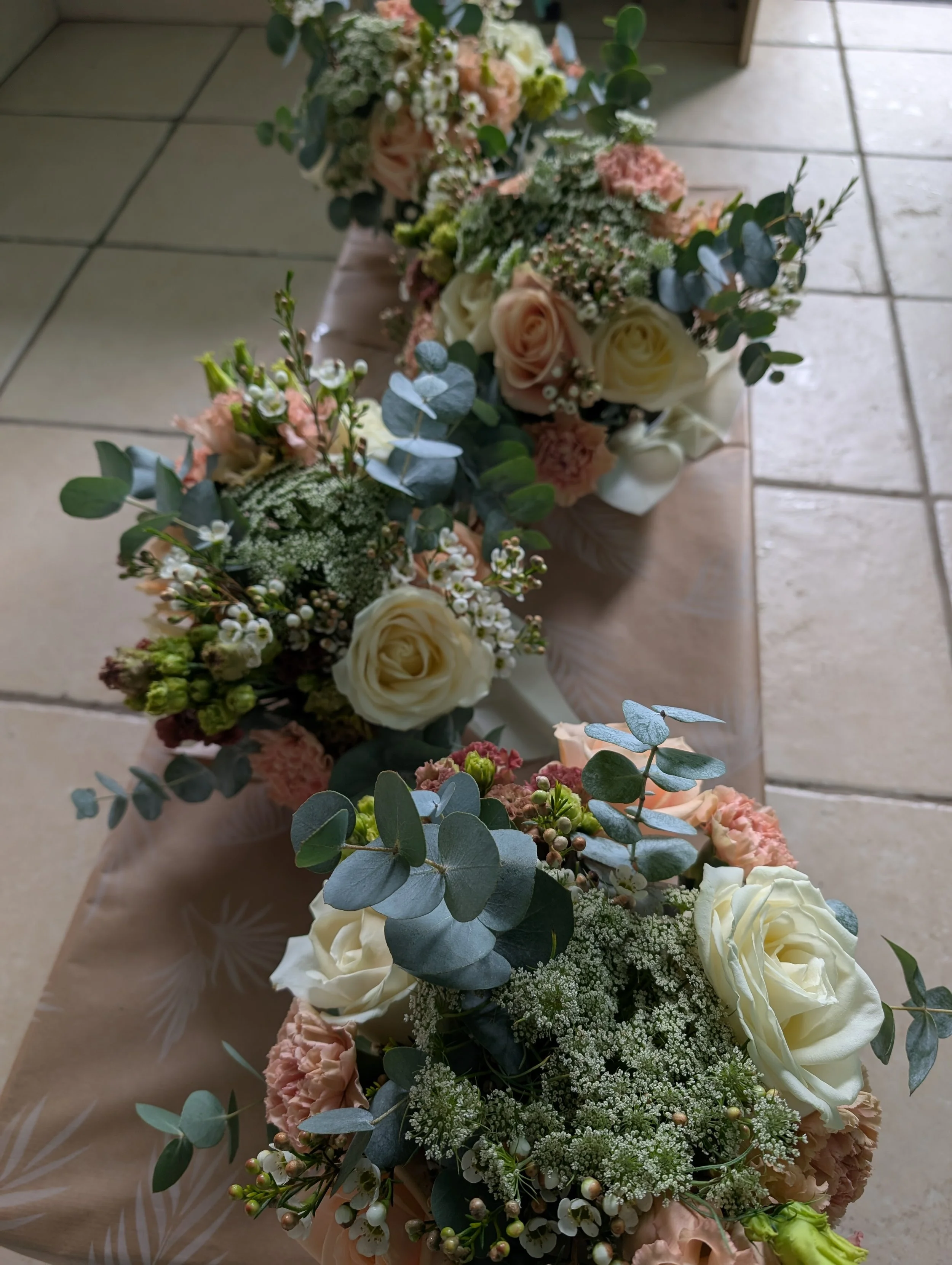 Close-up of a floral arrangement with white roses, pink carnations, baby's breath, eucalyptus, and other greenery on a tiled floor.