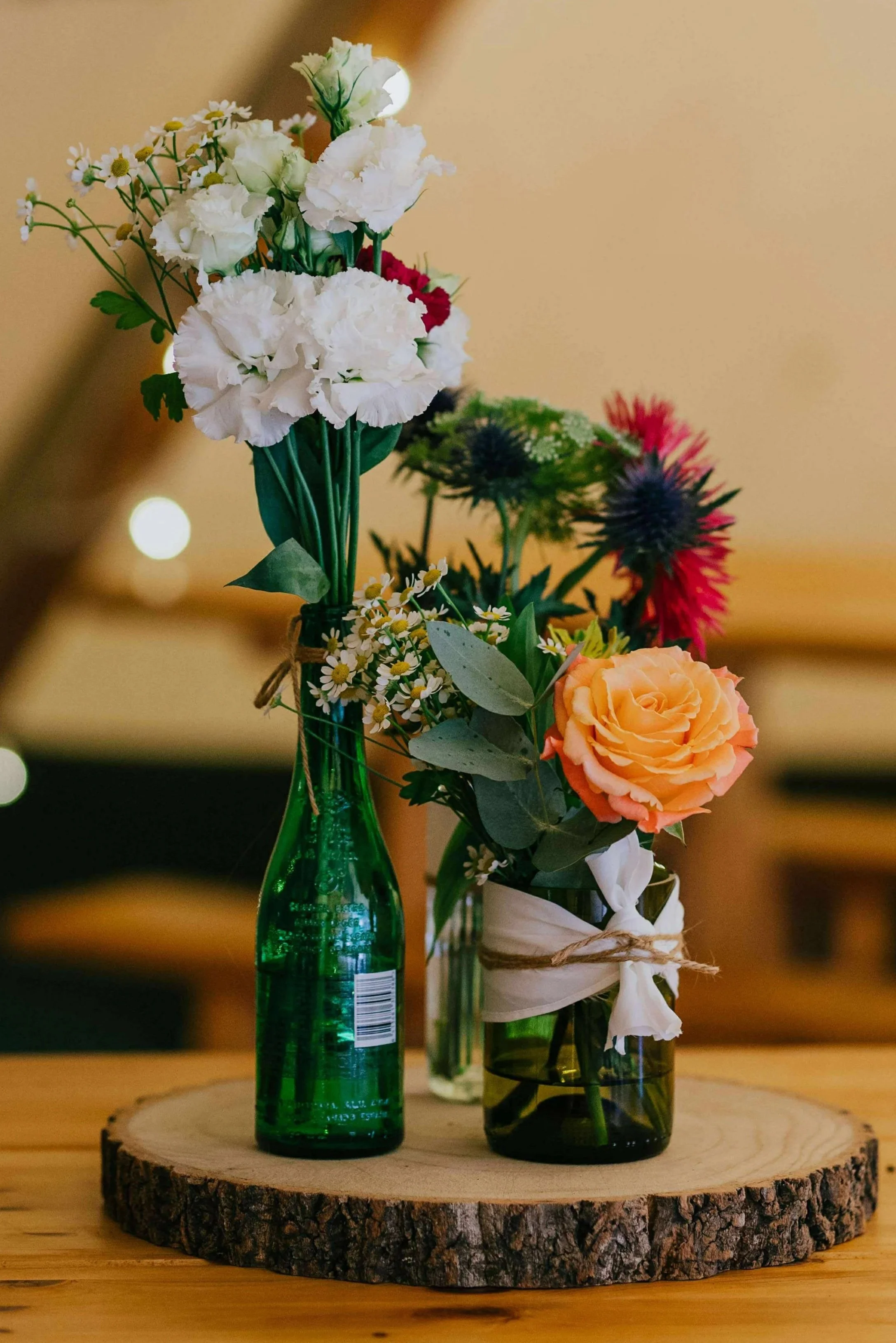 Two vases with colorful flowers on a wooden table with a wood slice base.