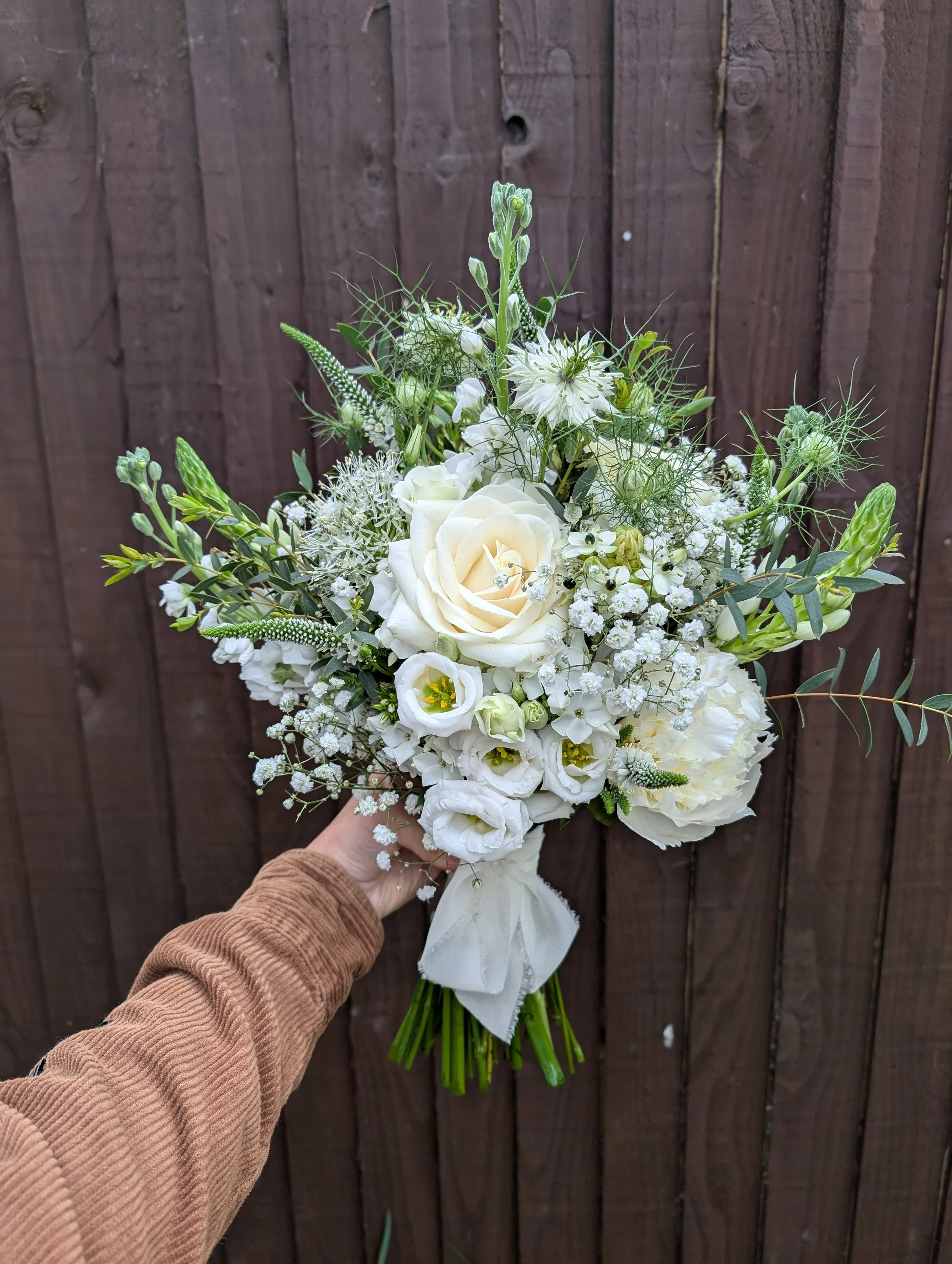 A hand holding a bouquet of white flowers in front of a wooden fence.