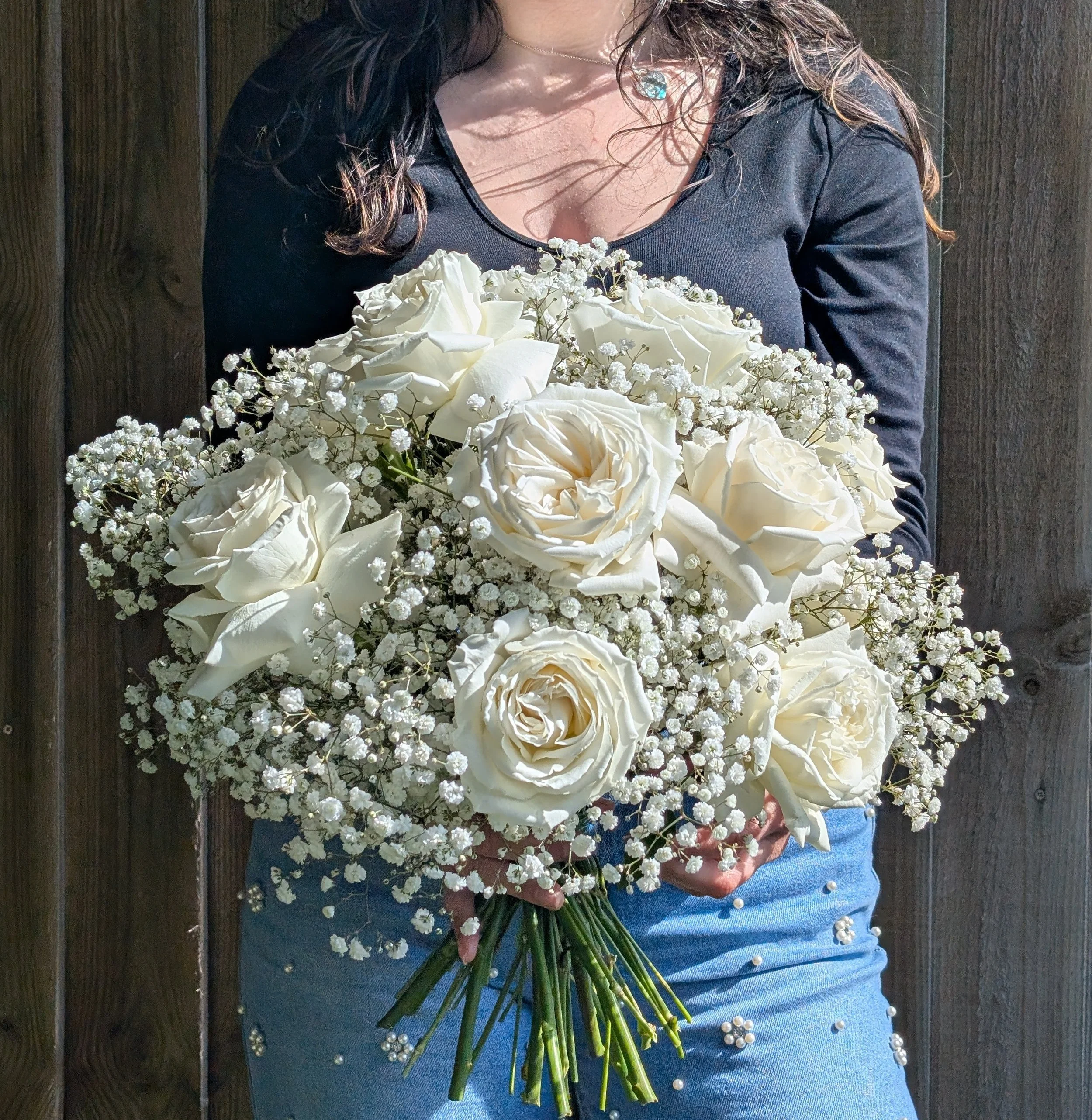 Person holding a bouquet of white roses and baby's breath flowers in front of a wooden fence.