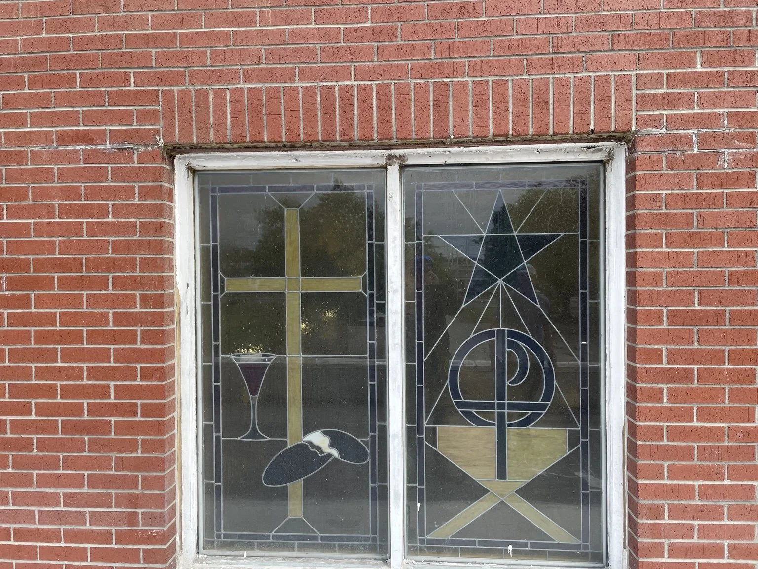 Stained-glass church window with religious symbols set in a red brick wall.