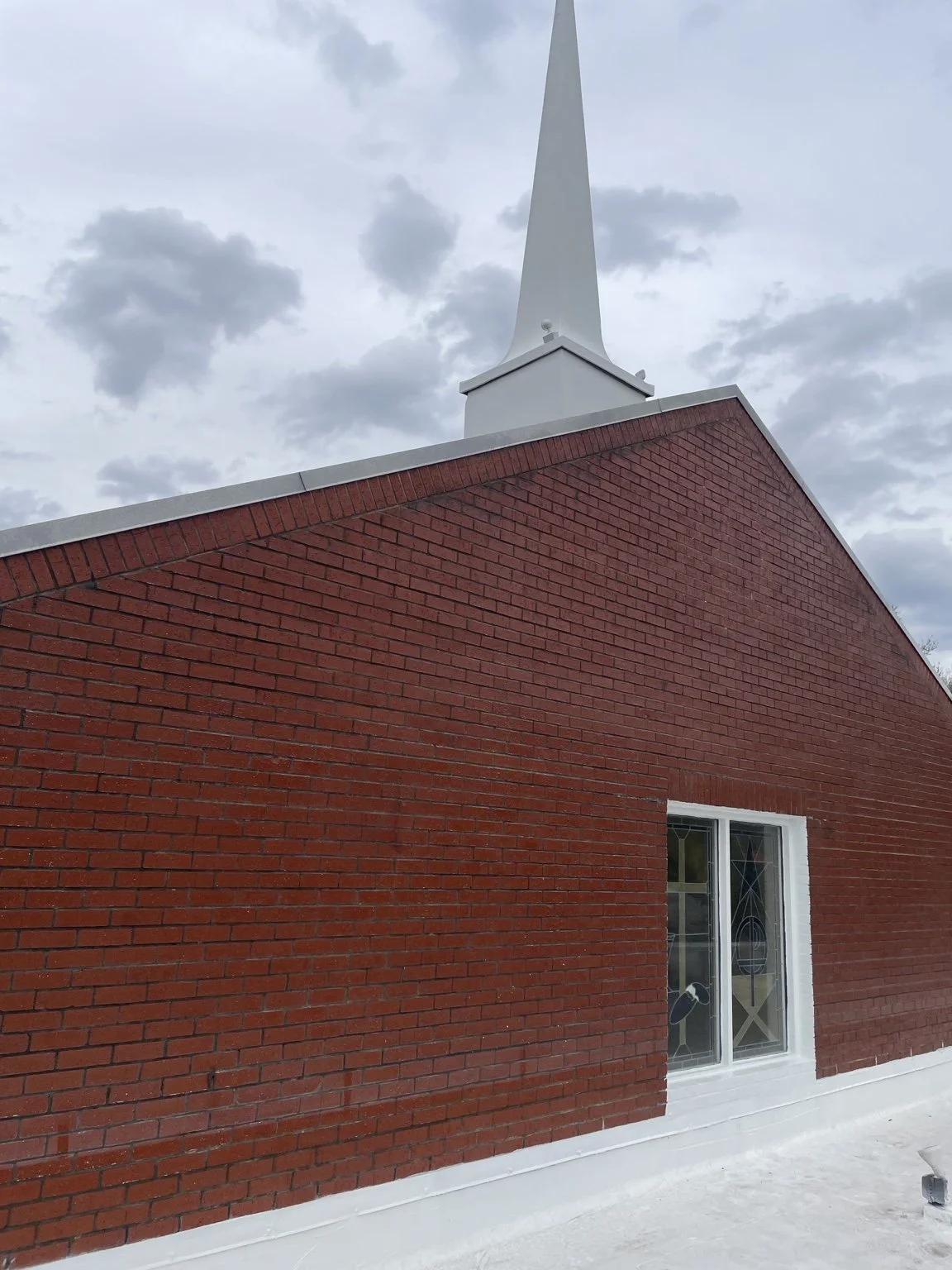 Red brick church building with a white steeple under a cloudy sky.