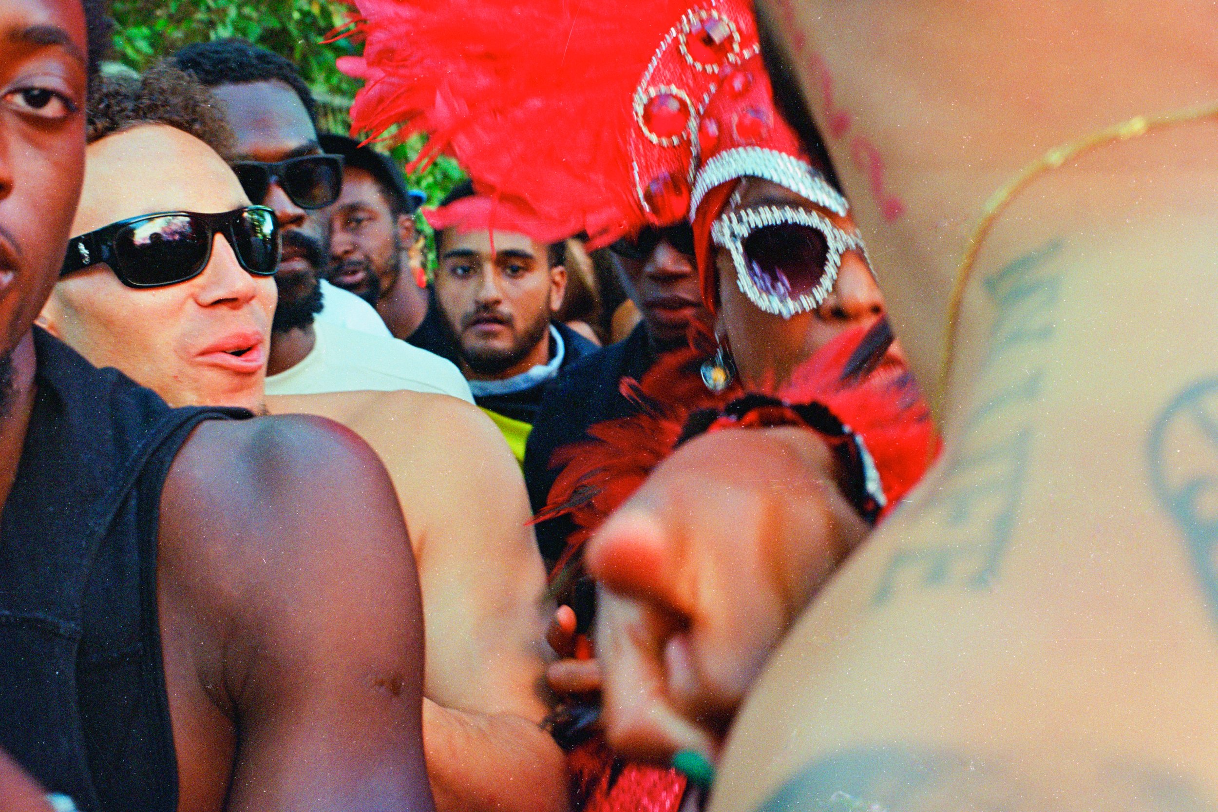 A crowd of people gathered close together, some wearing dark sunglasses, in what appears to be a lively outdoor event.