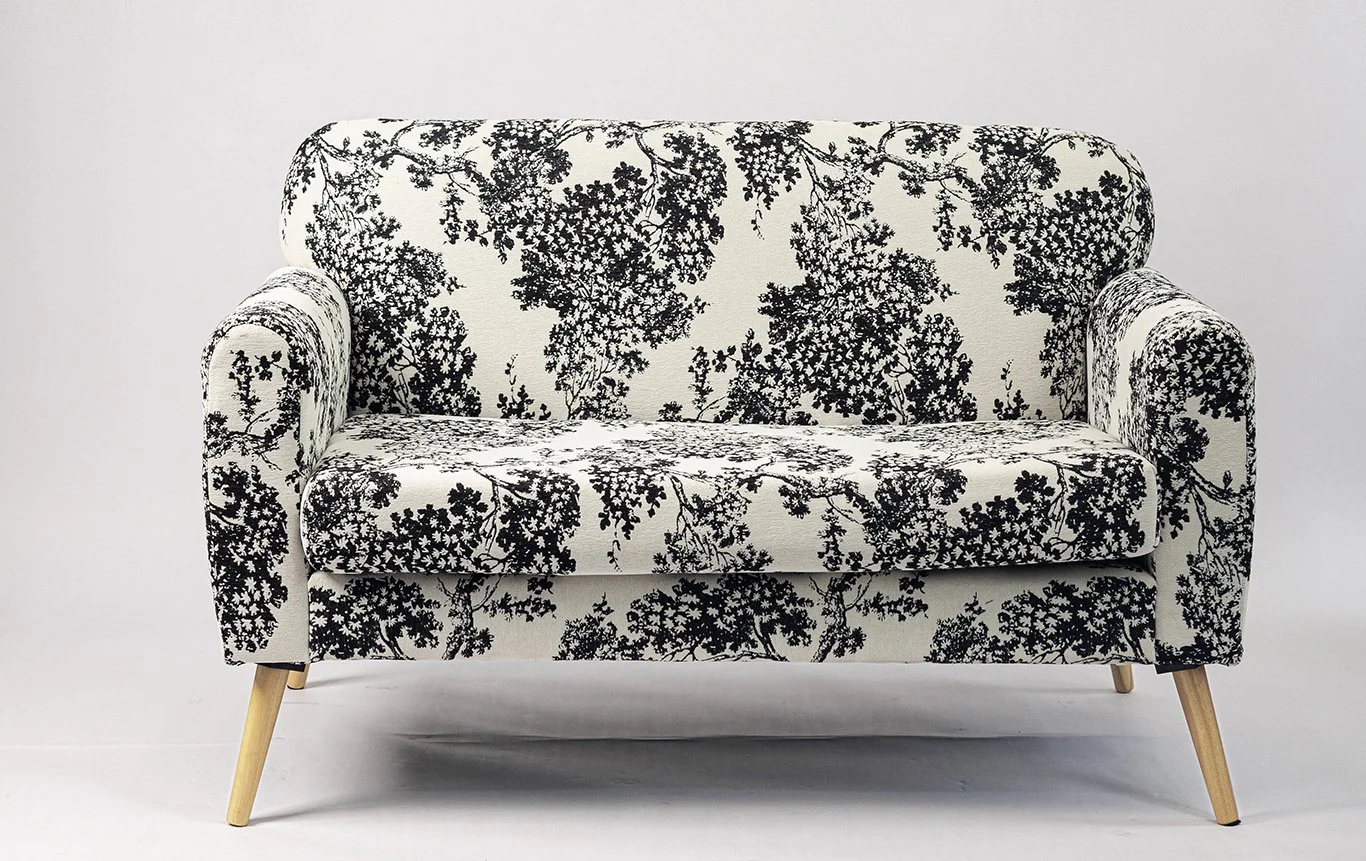 Black and white floral patterned upholstered sofa with angled wooden legs against a plain white background.