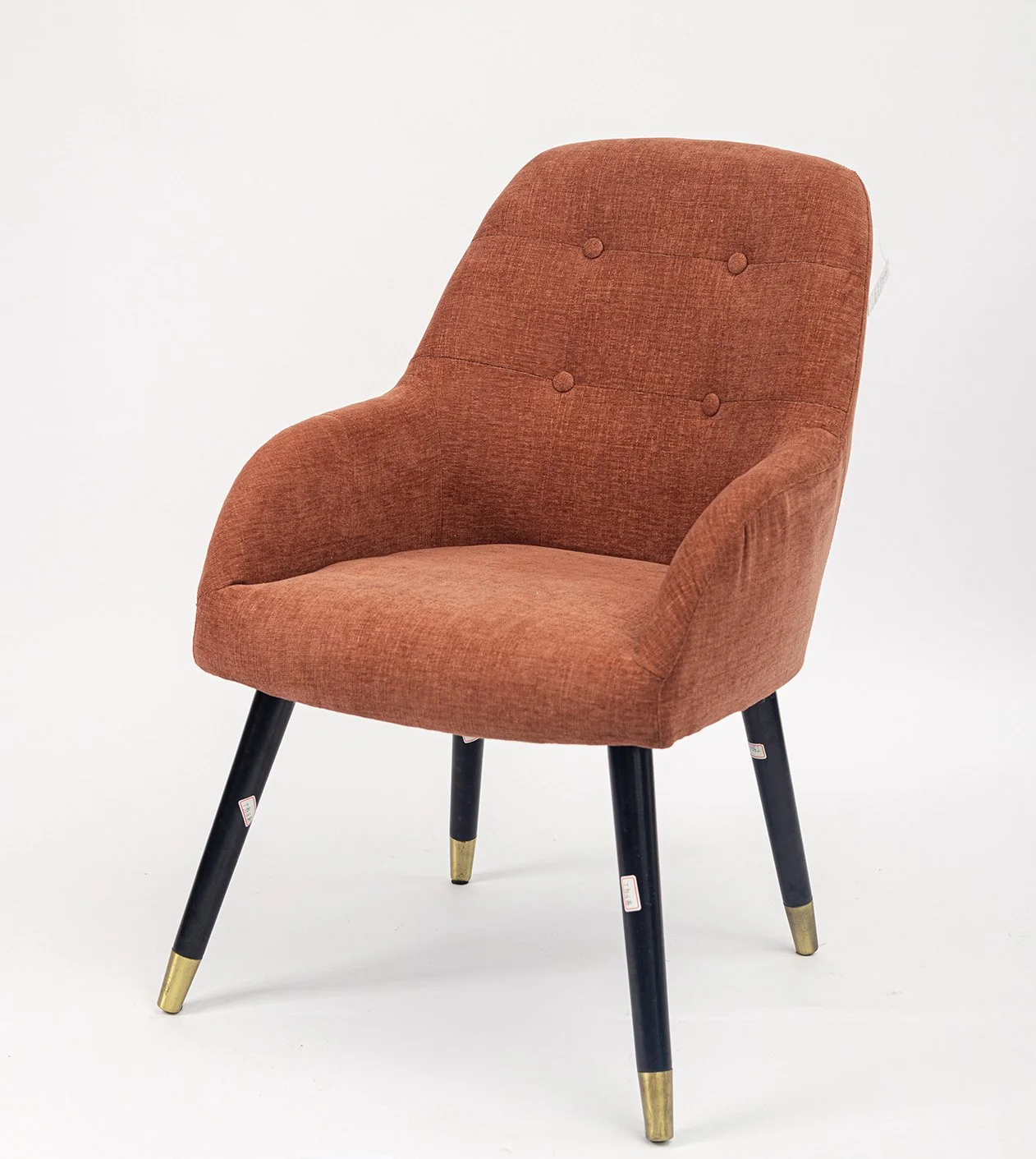 A mid-century modern style armchair with a rust-colored upholstered seat and backrest, black tapered legs with gold caps, set against a plain white background.