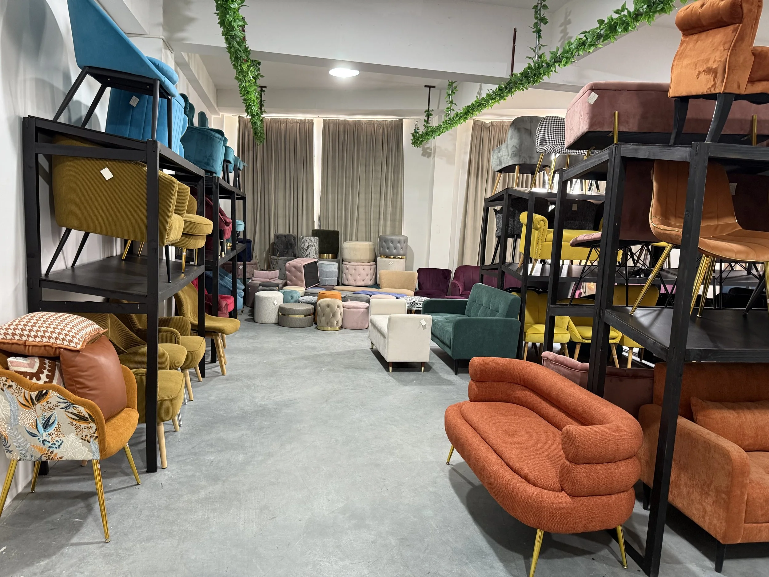 A furniture store displays a variety of colorful chairs, sofas, and ottomans arranged on shelves and on the floor, with beige curtains in the background.