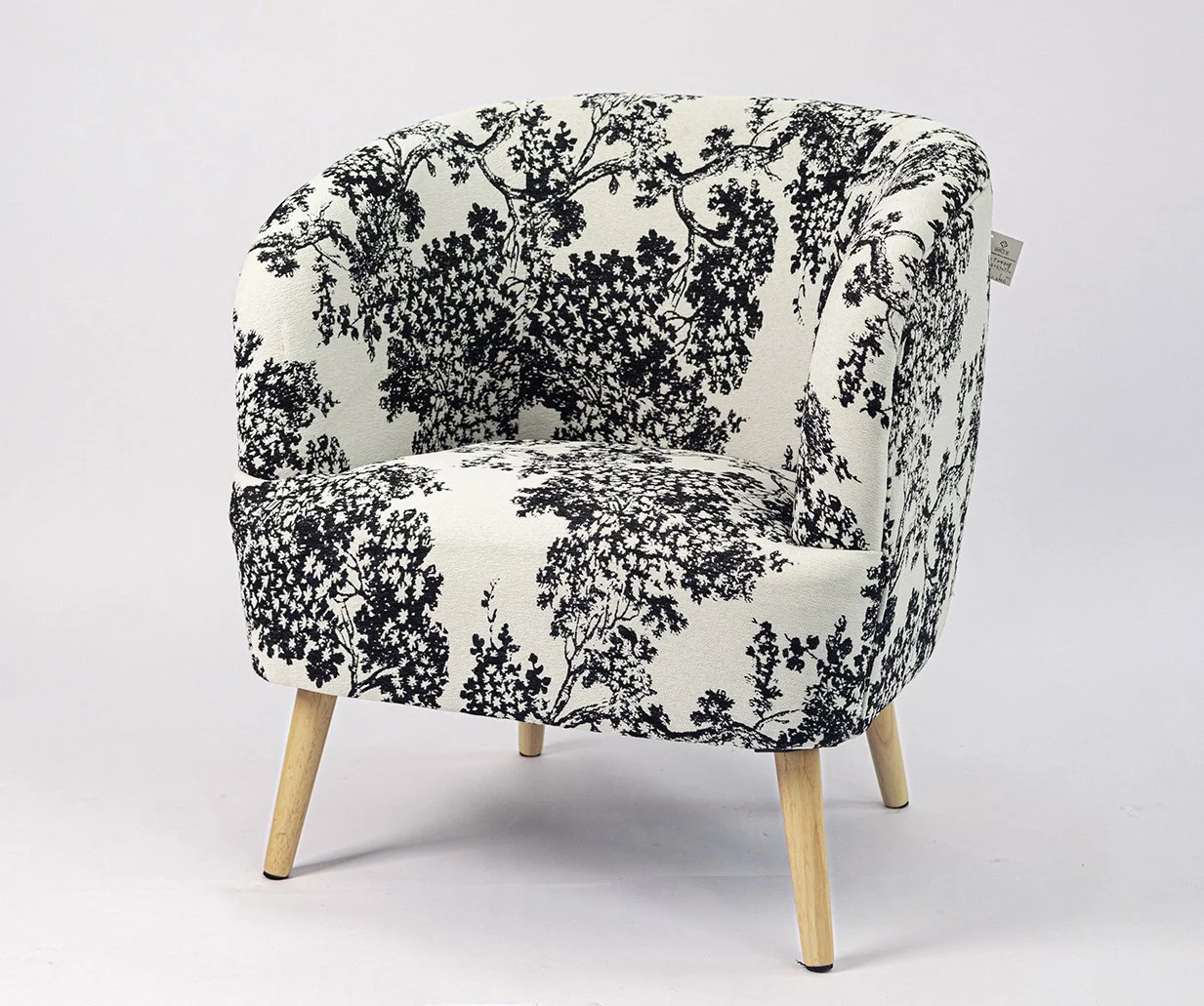 A white upholstered armchair with black floral pattern, angled wooden legs, against a plain light background.