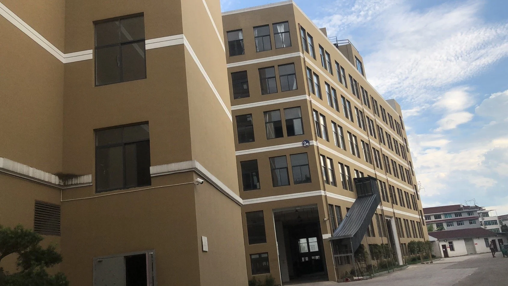 Multi-story beige apartment building with black windows and an external staircase, under a partly cloudy sky.
