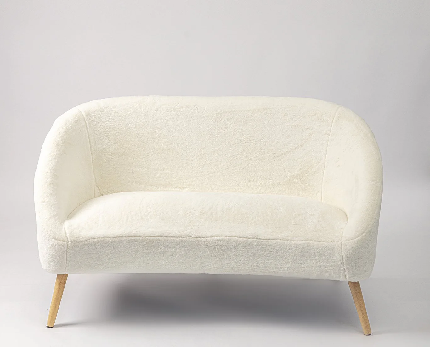 A small, cream-colored, fabric-covered sofa with wooden legs placed against a plain, light gray background.
