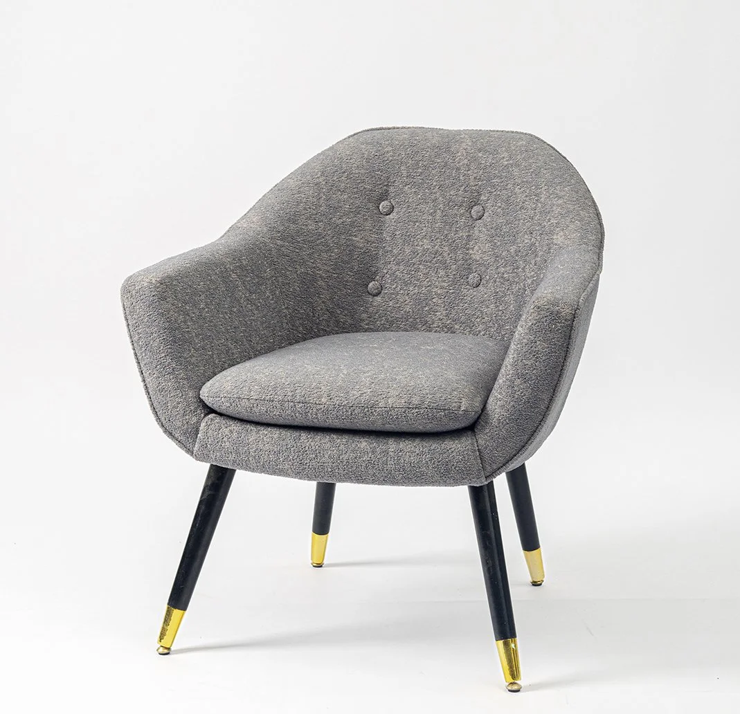 A modern gray upholstered armchair with black legs and gold tips on the legs, set against a plain white background.