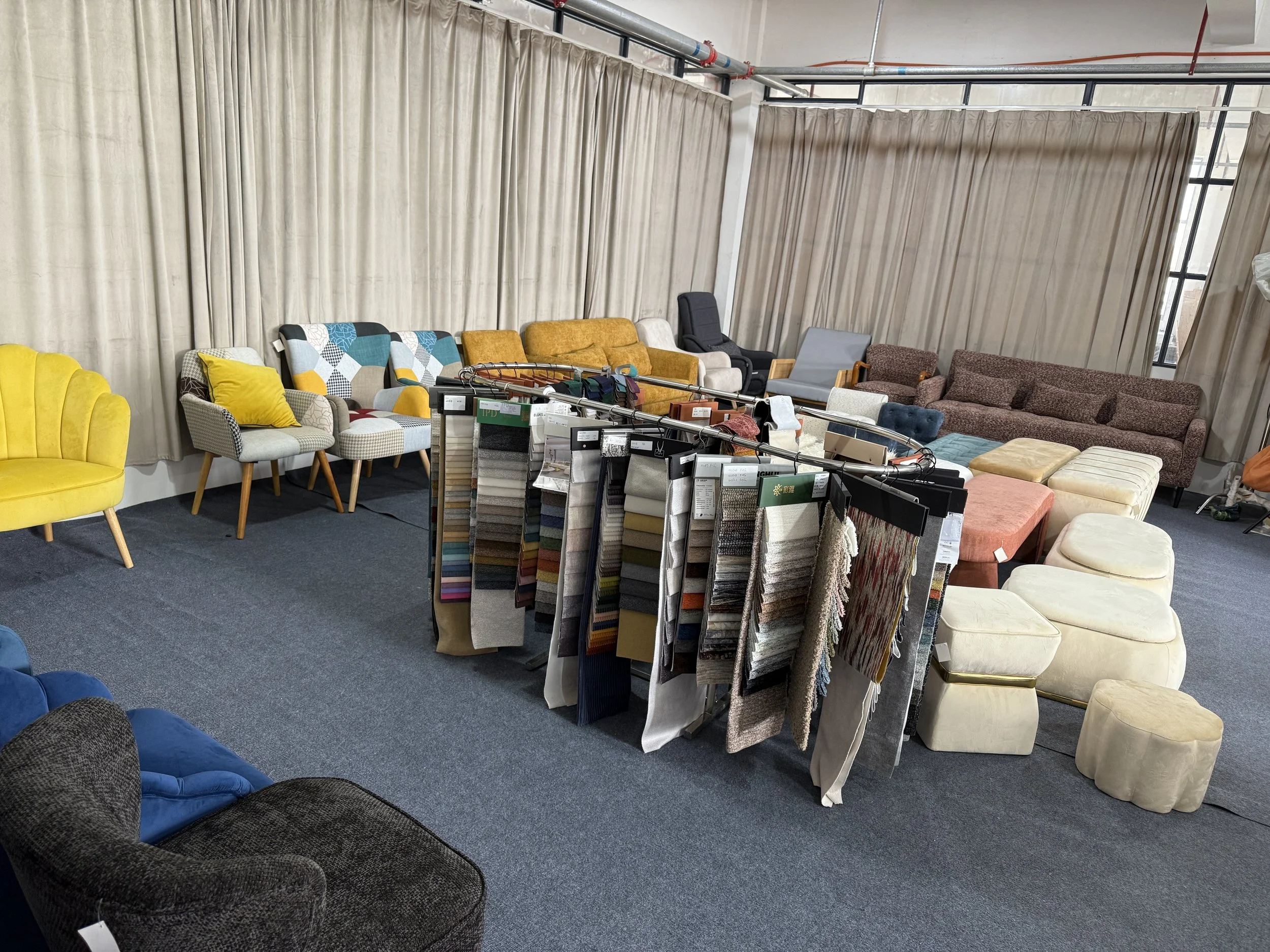Showroom with various sofas and chairs arranged around and in front of beige curtains, with fabric samples hanging in the center.