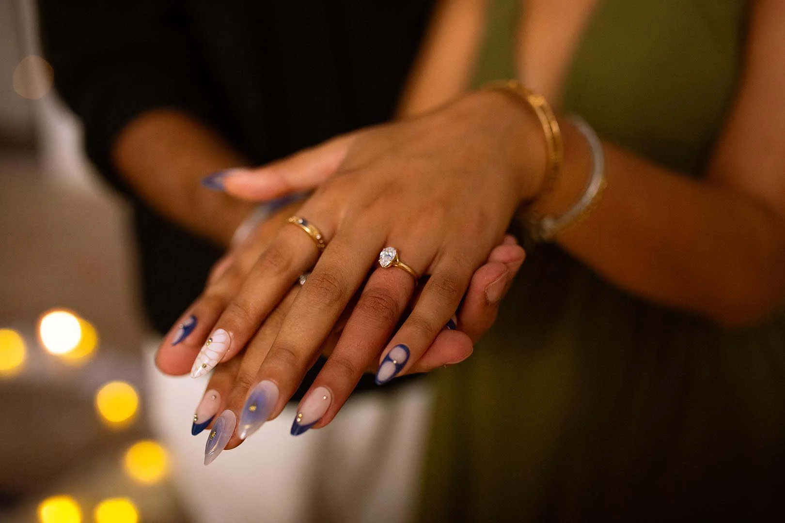 A close-up of intertwined hands with a proposal ring in focus.