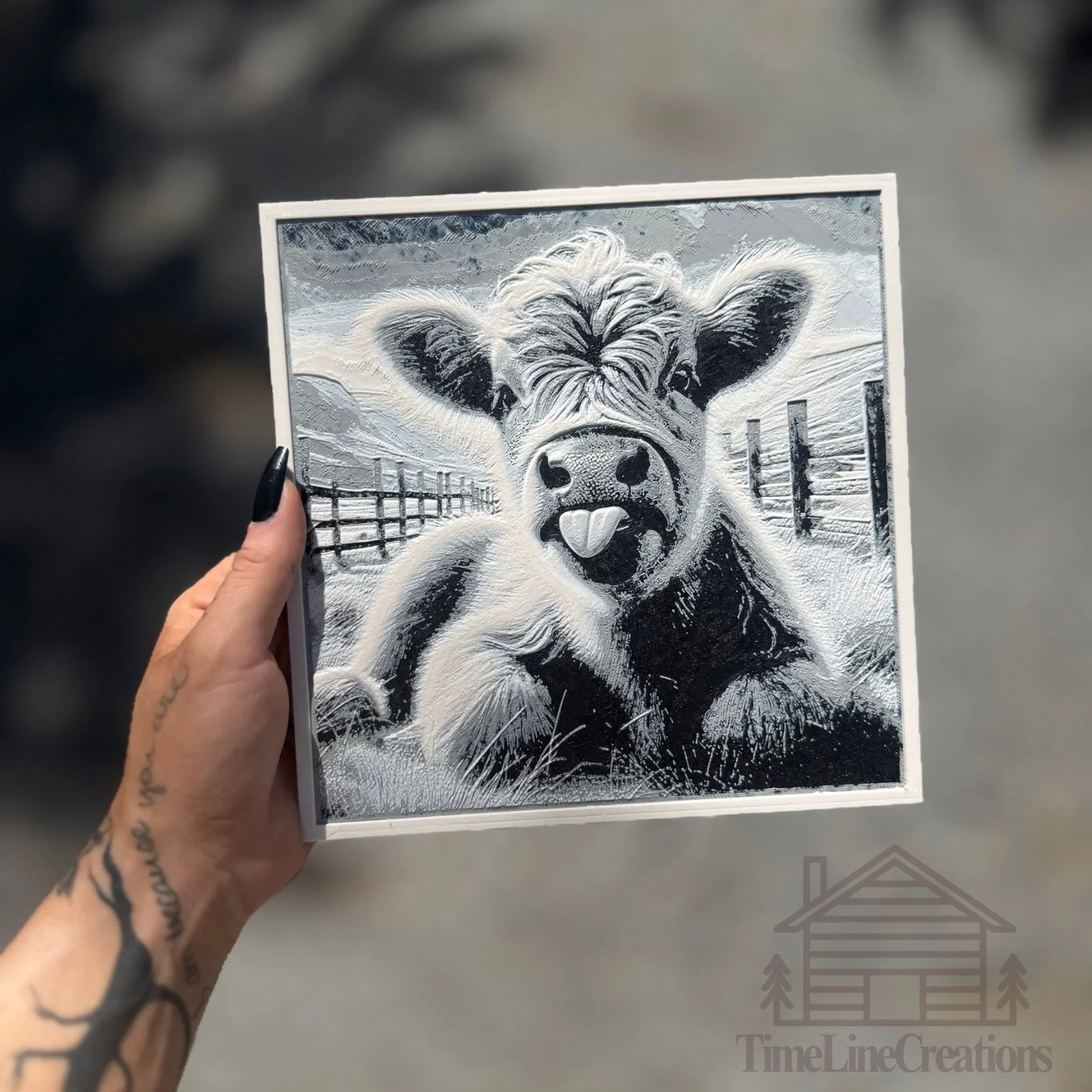 A black and white painted portrait of a calf with its tongue out, set against a rural background with a fence and sky.