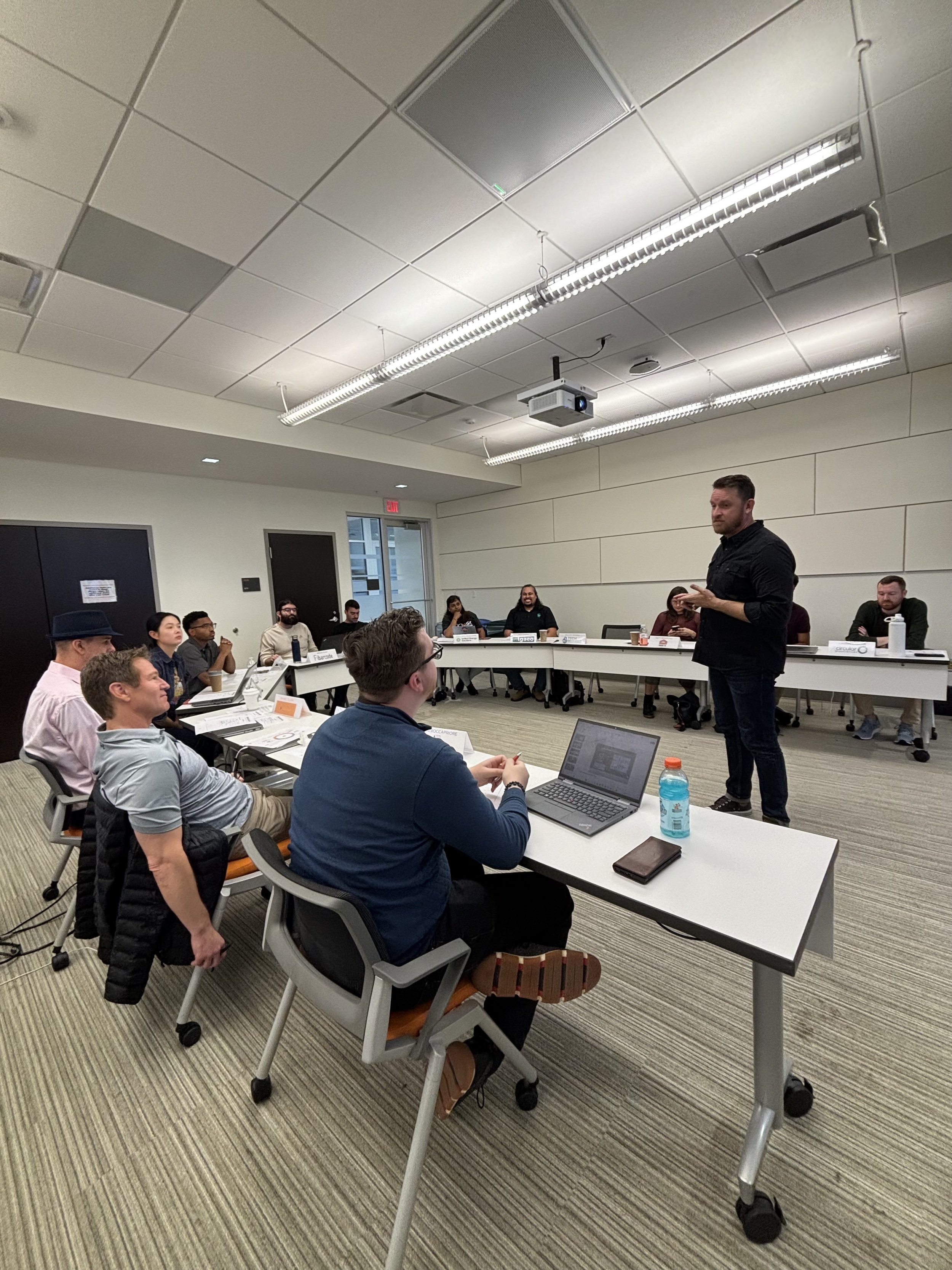 Chris McAdoo speaking to a group of entrepreneurs in the Spark Cleantech Accelerator - seated in a U-shaped conference room. The participants are listening and have laptops and notebooks in front of them.