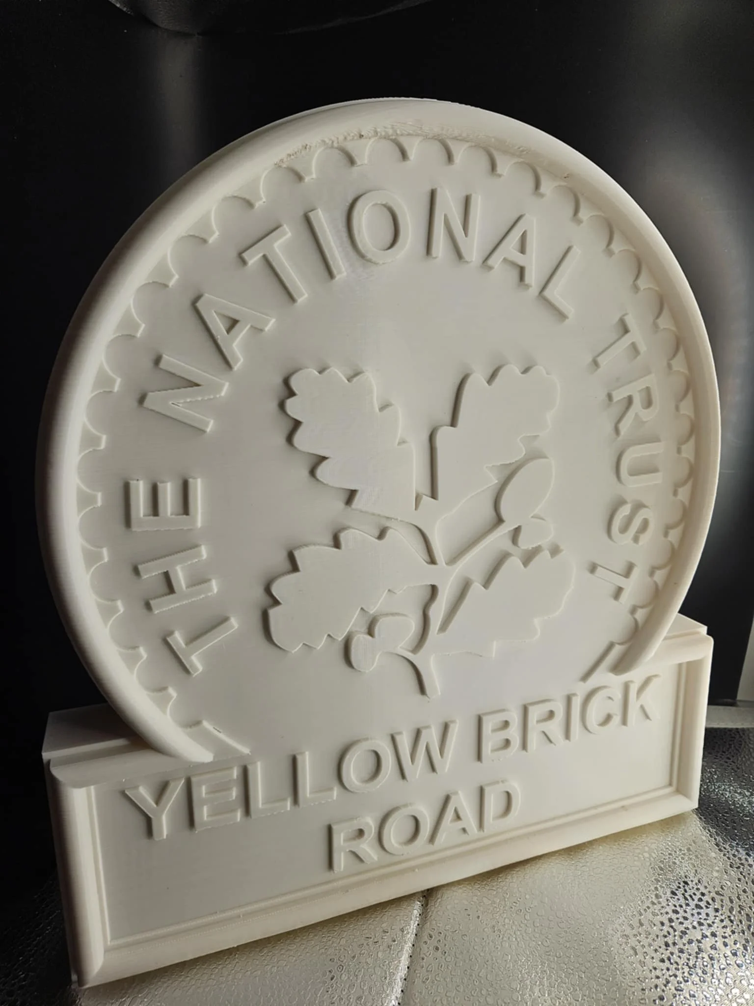 White 3D printed sign with the words "The National Trust" and "Yellow Brick Road," featuring a leaf design in the center.