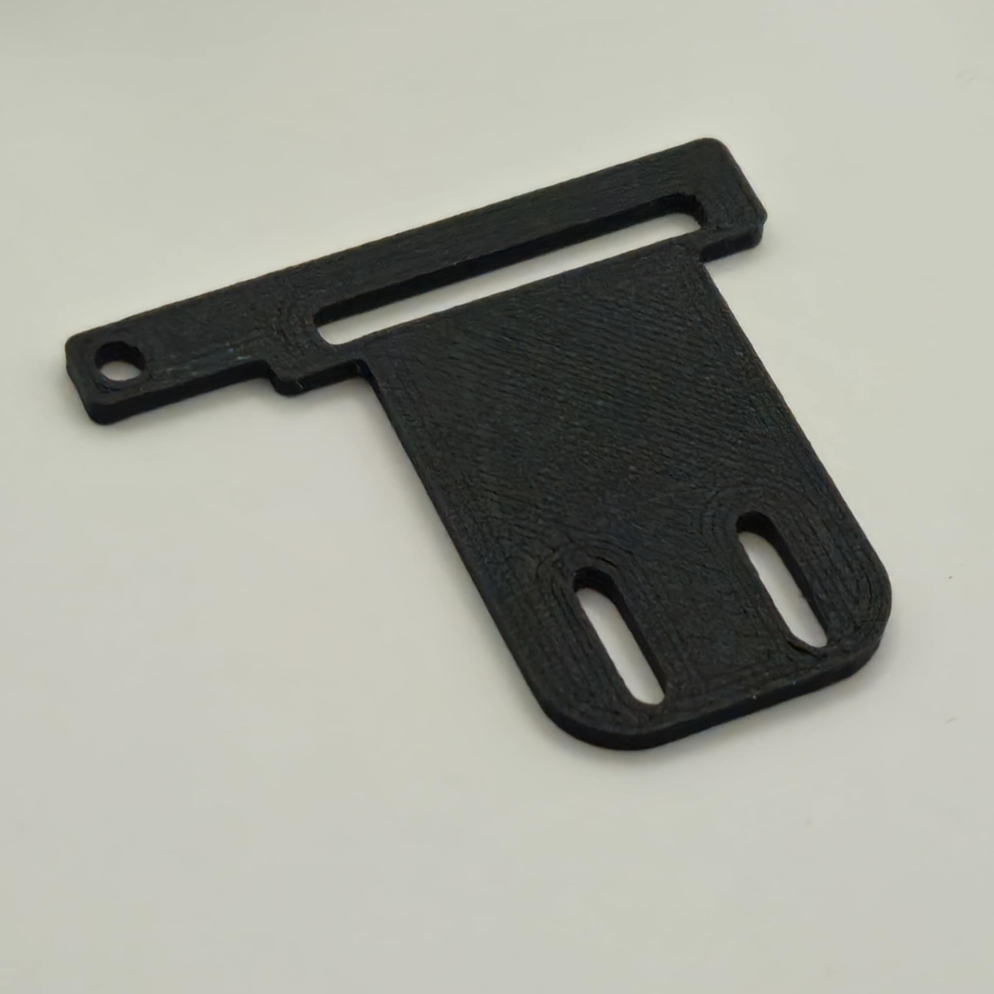 Black plastic 3D printed part with slots on a white background.