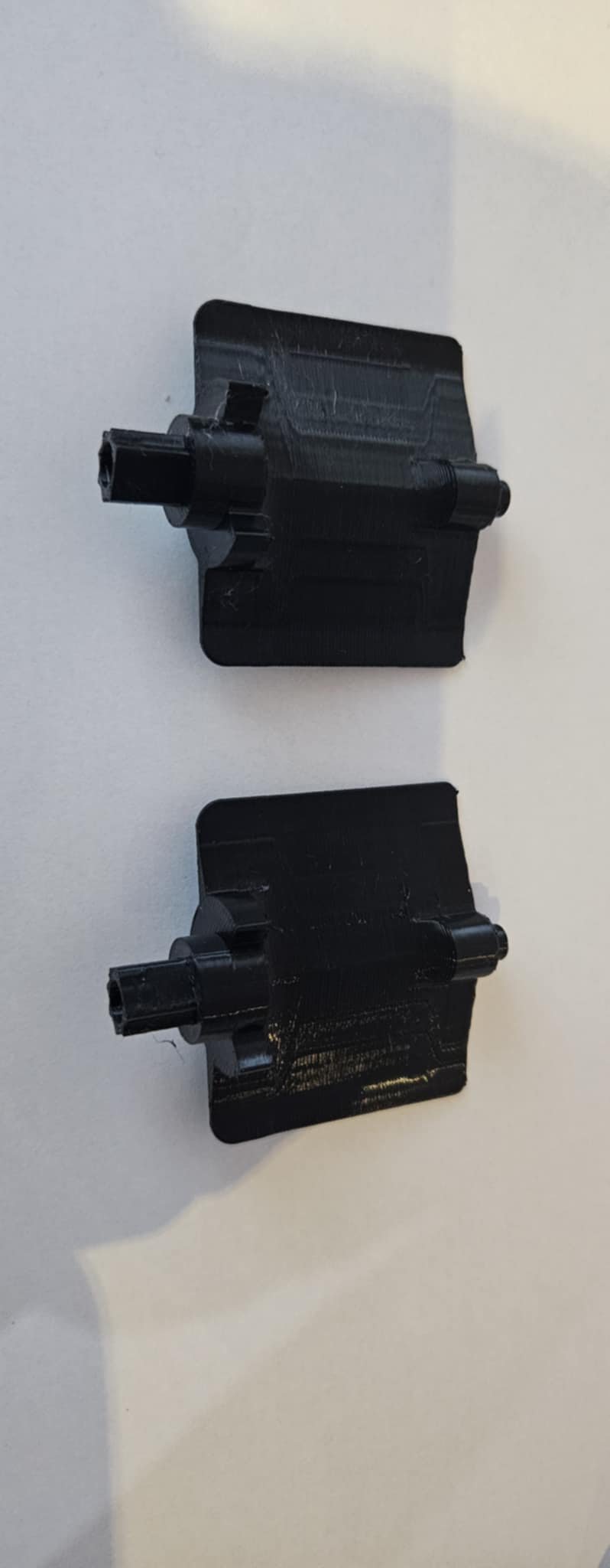 Two black 3D-printed plastic parts with cylindrical extensions on a white background.
