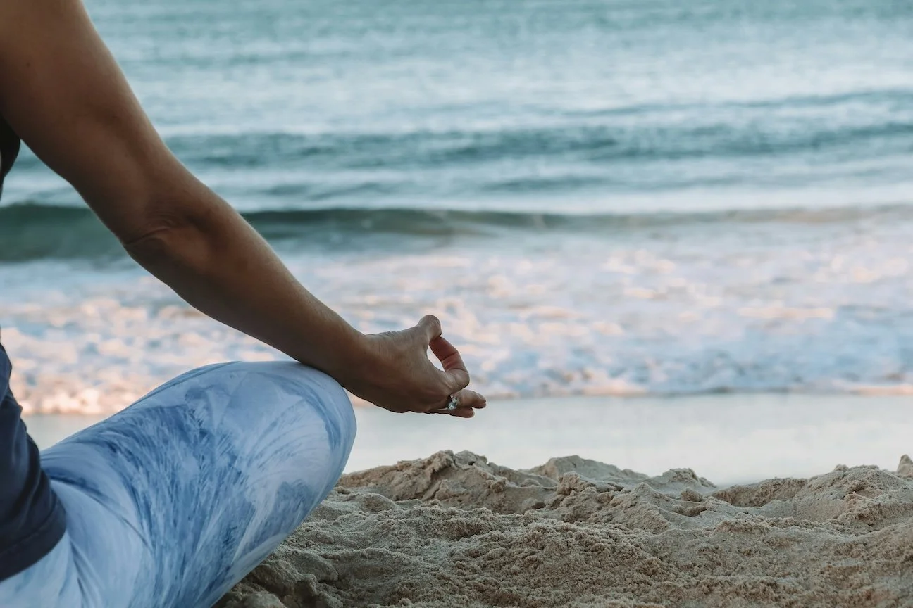 Person practicing mindfulness meditation on the beach, supporting emotional regulation and mental health through mindfulness based therapy