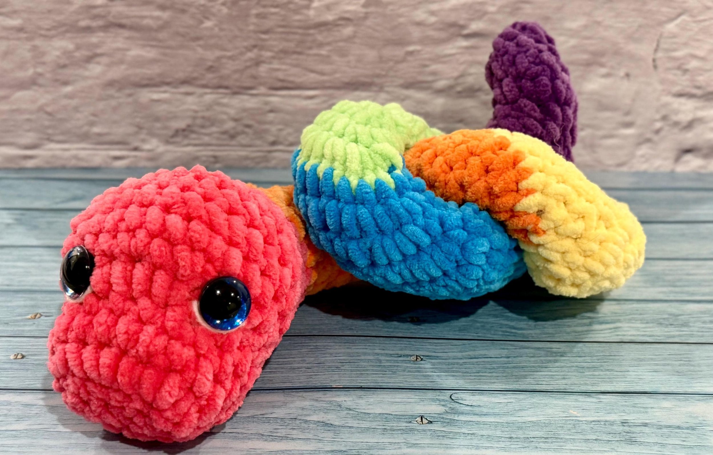 Handmade crochet snake plushie in vibrant multicolor design, a fun gift for reptile lovers.