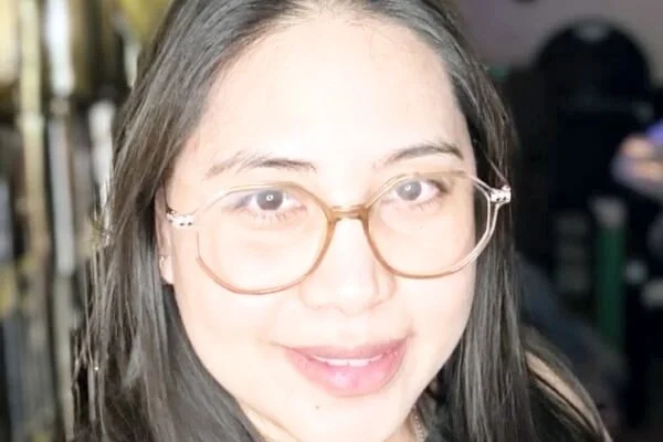 A woman with long, dark hair and glasses smiling at the camera.